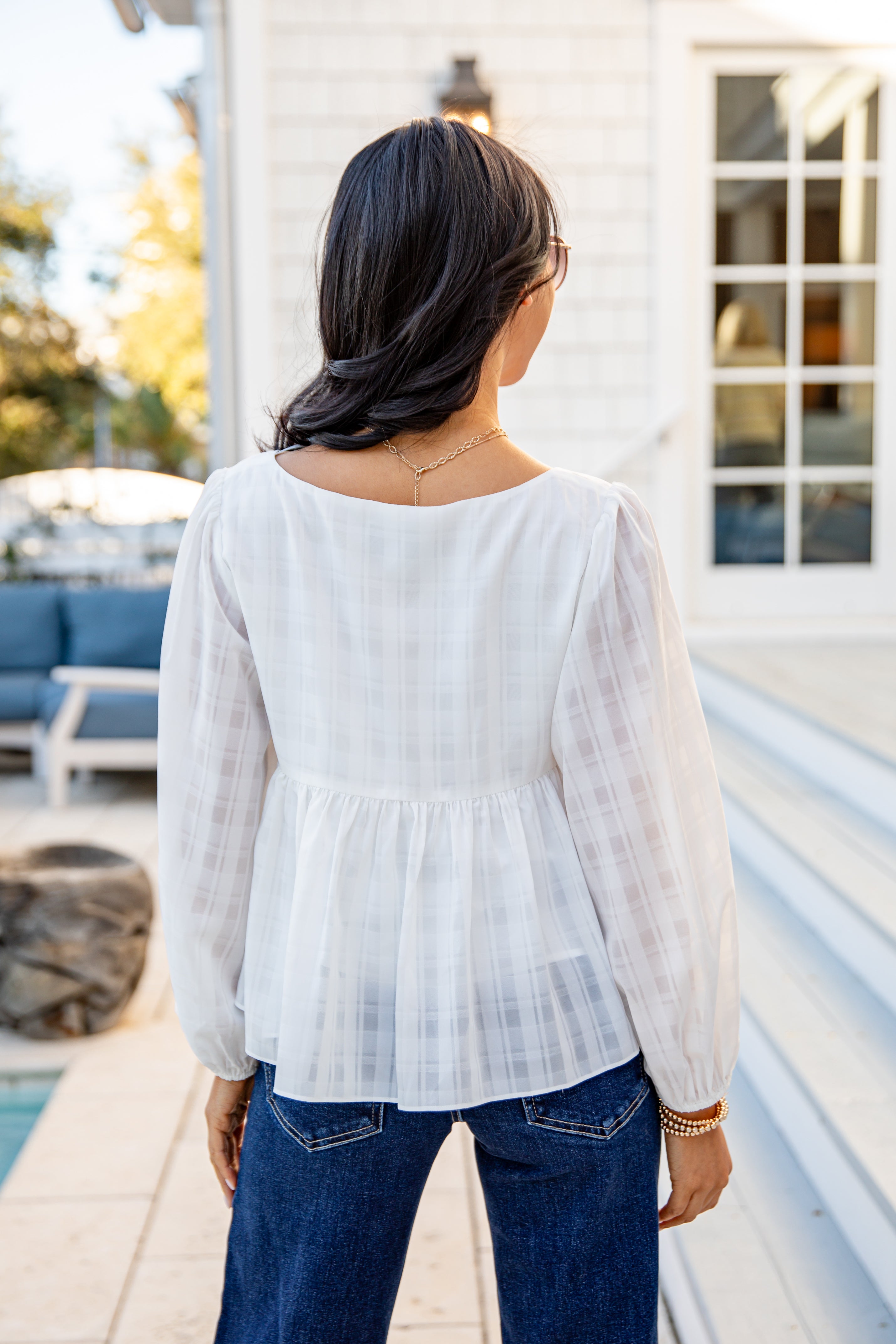 Woman wearing a white blouse and blue jeans standing by a poolside.