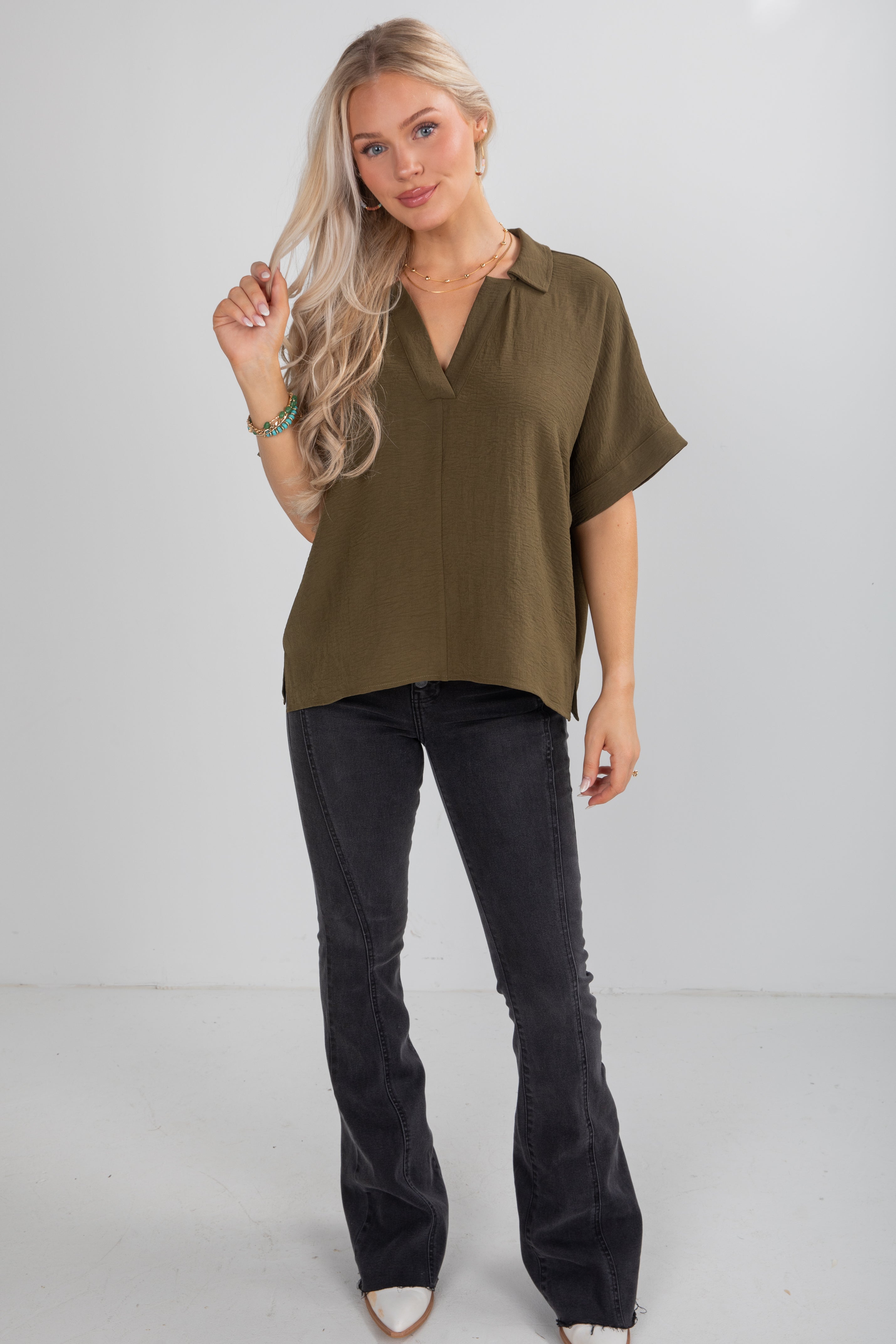 Woman wearing an olive green blouse and black pants on a white background