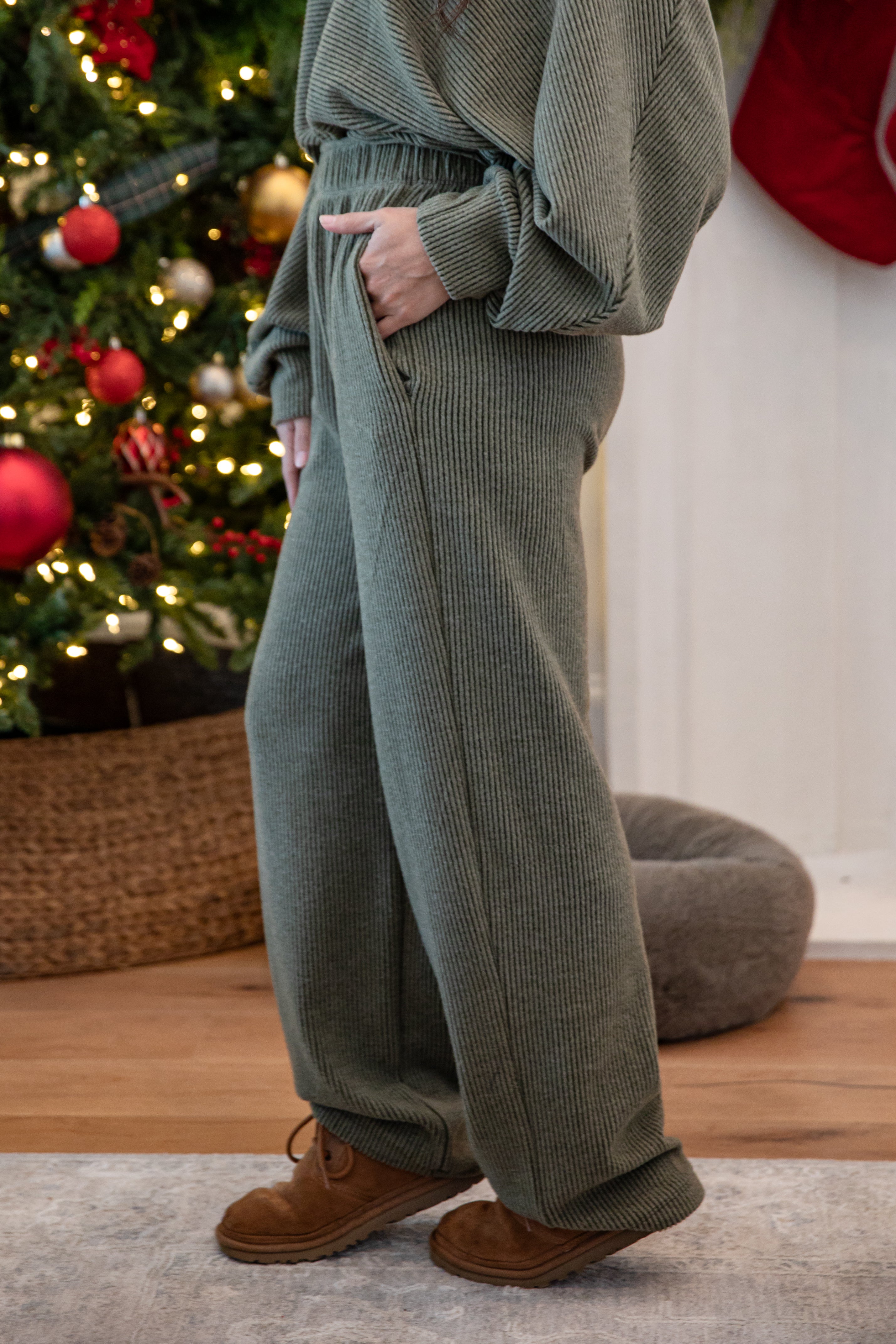 Person wearing green corduroy pants standing in front of a decorated Christmas tree.