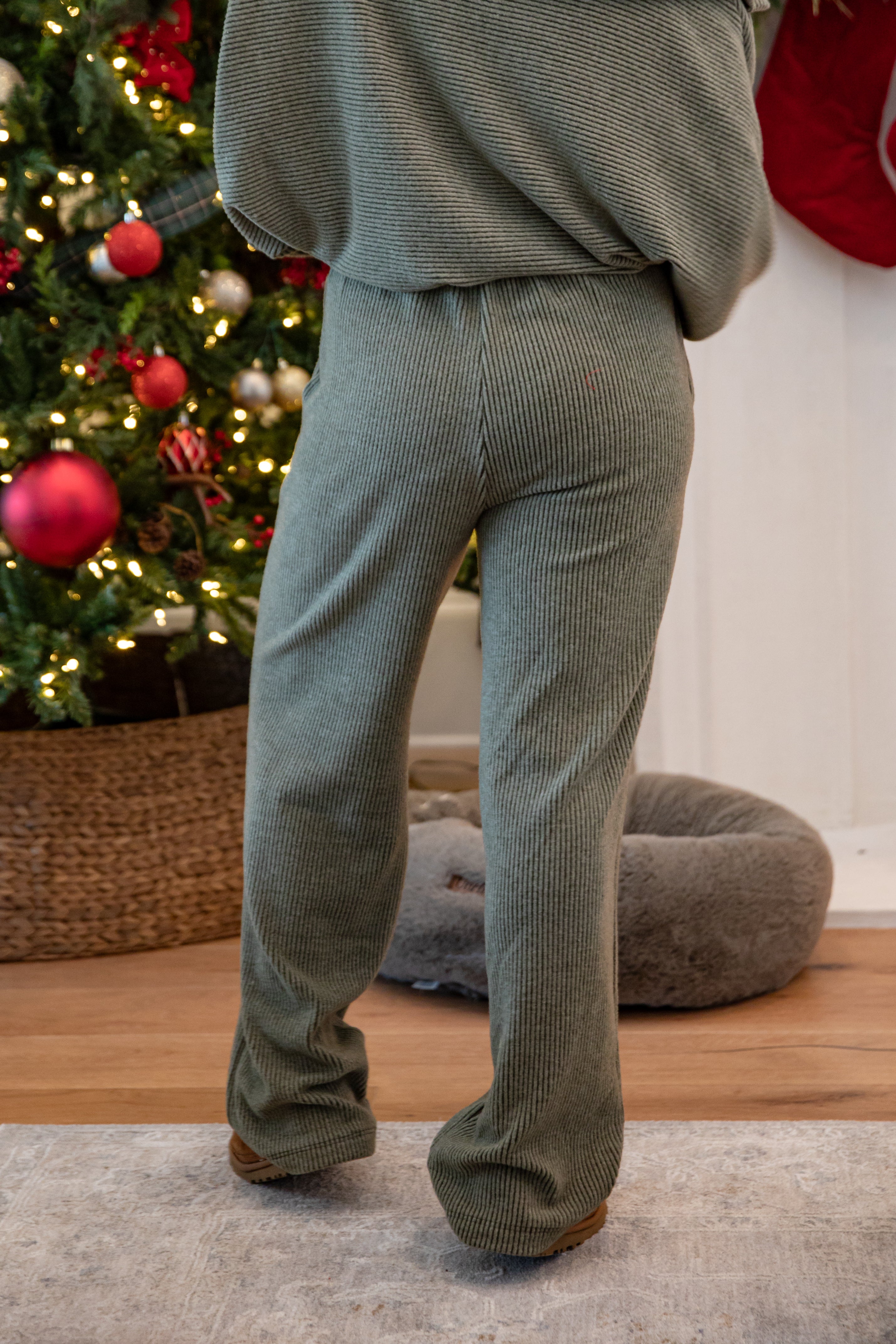 Person wearing a green outfit standing in front of a decorated Christmas tree.