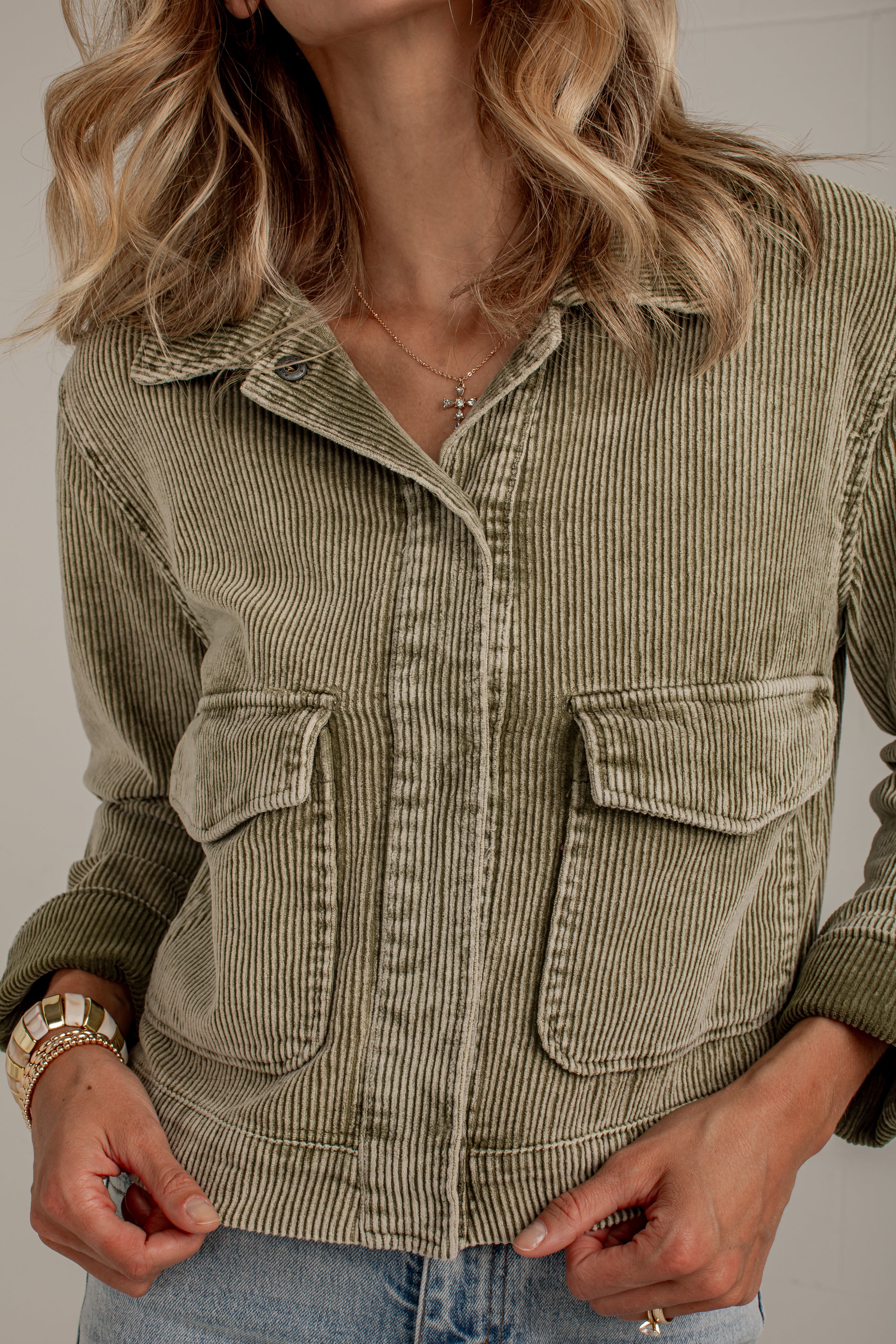 A woman wearing an olive green corduroy jacket with front flap pockets, paired with light blue jeans. The photo is a close-up crop showing the texture of the corduroy and the fit of the jacket.