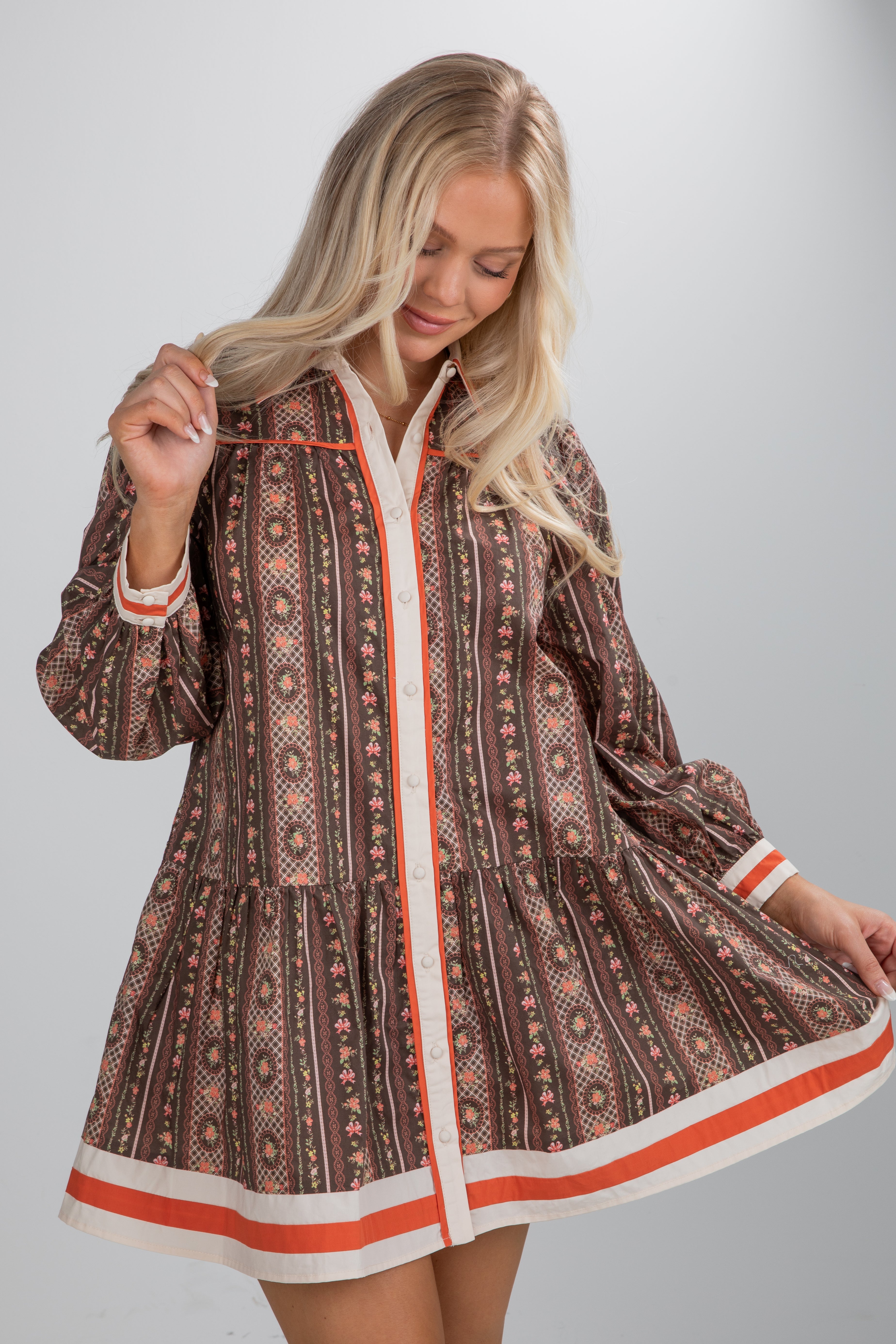 Woman wearing a patterned dress with orange trim on a plain background