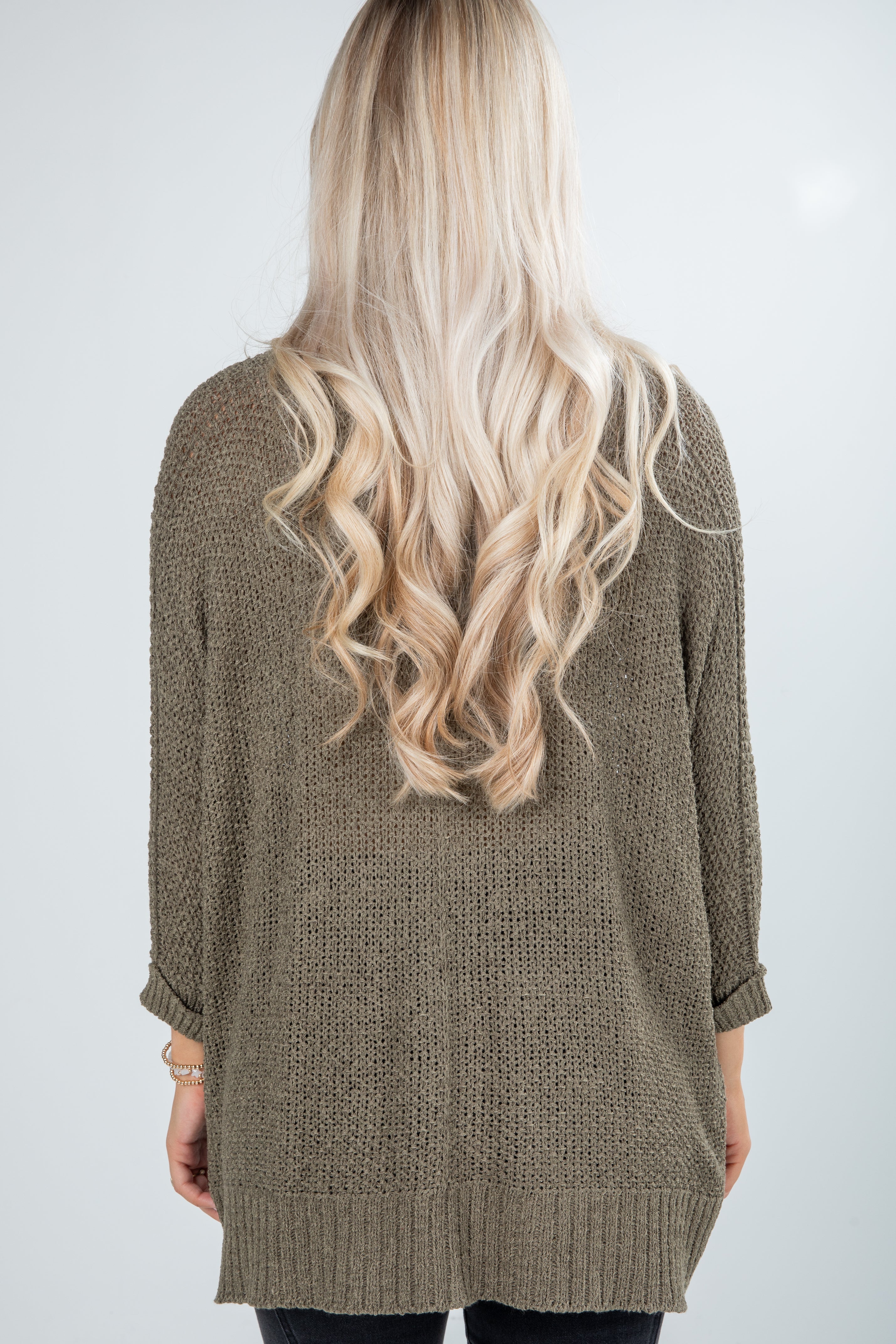 Person wearing a brown knitted cardigan with long blonde hair on a white background