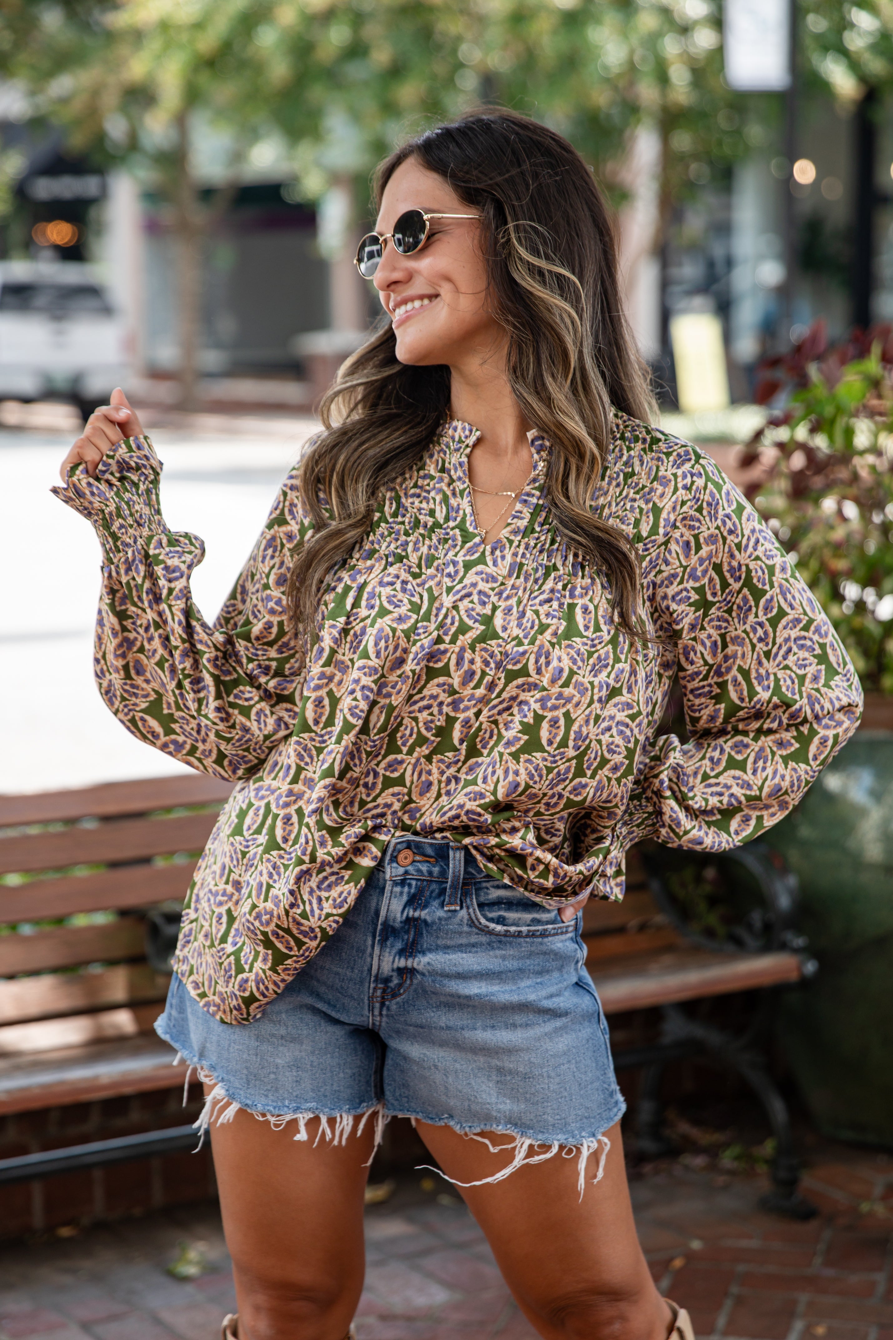 Woman wearing a patterned blouse and denim shorts outdoors.
