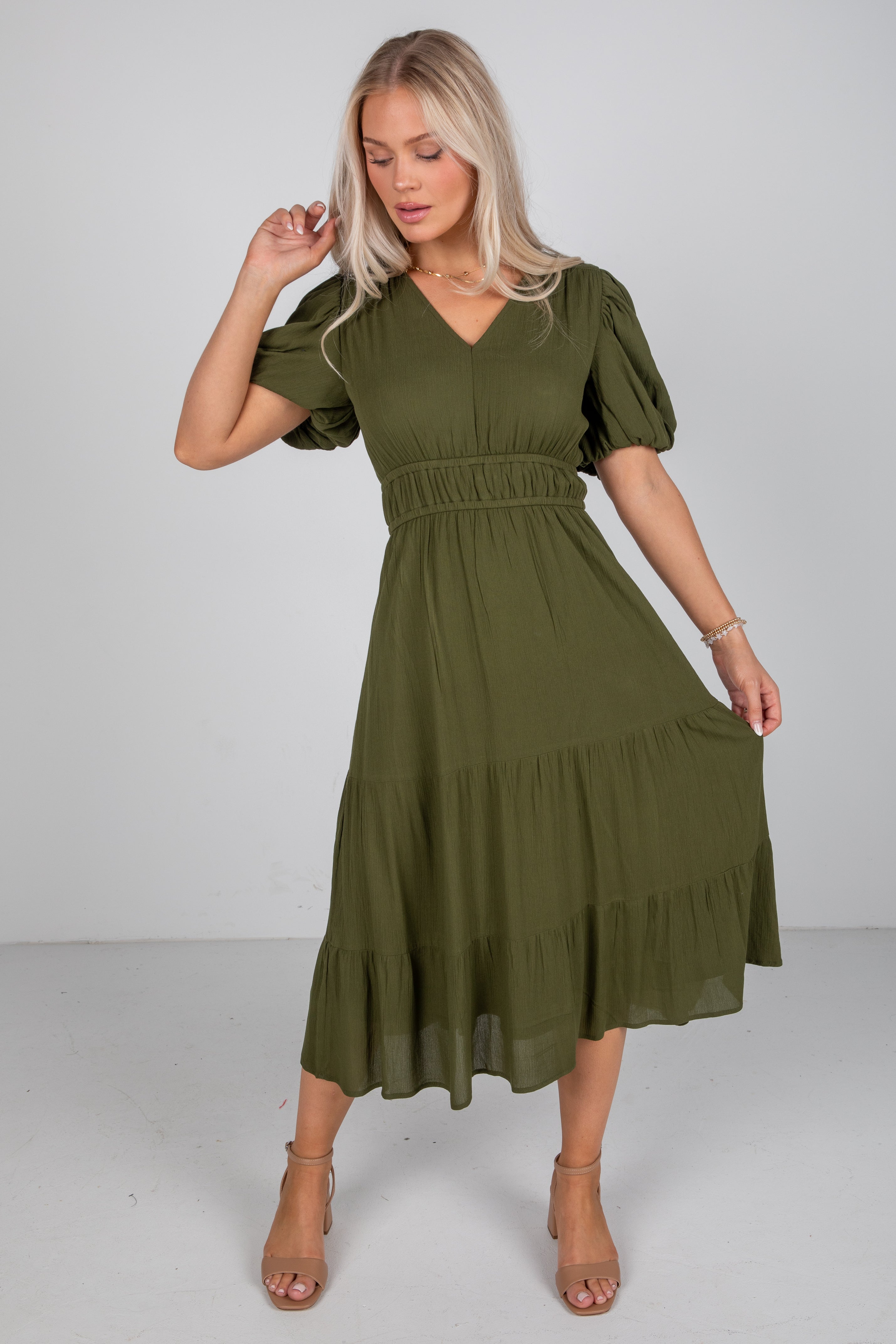 Woman wearing an olive green dress with puff sleeves on a white background