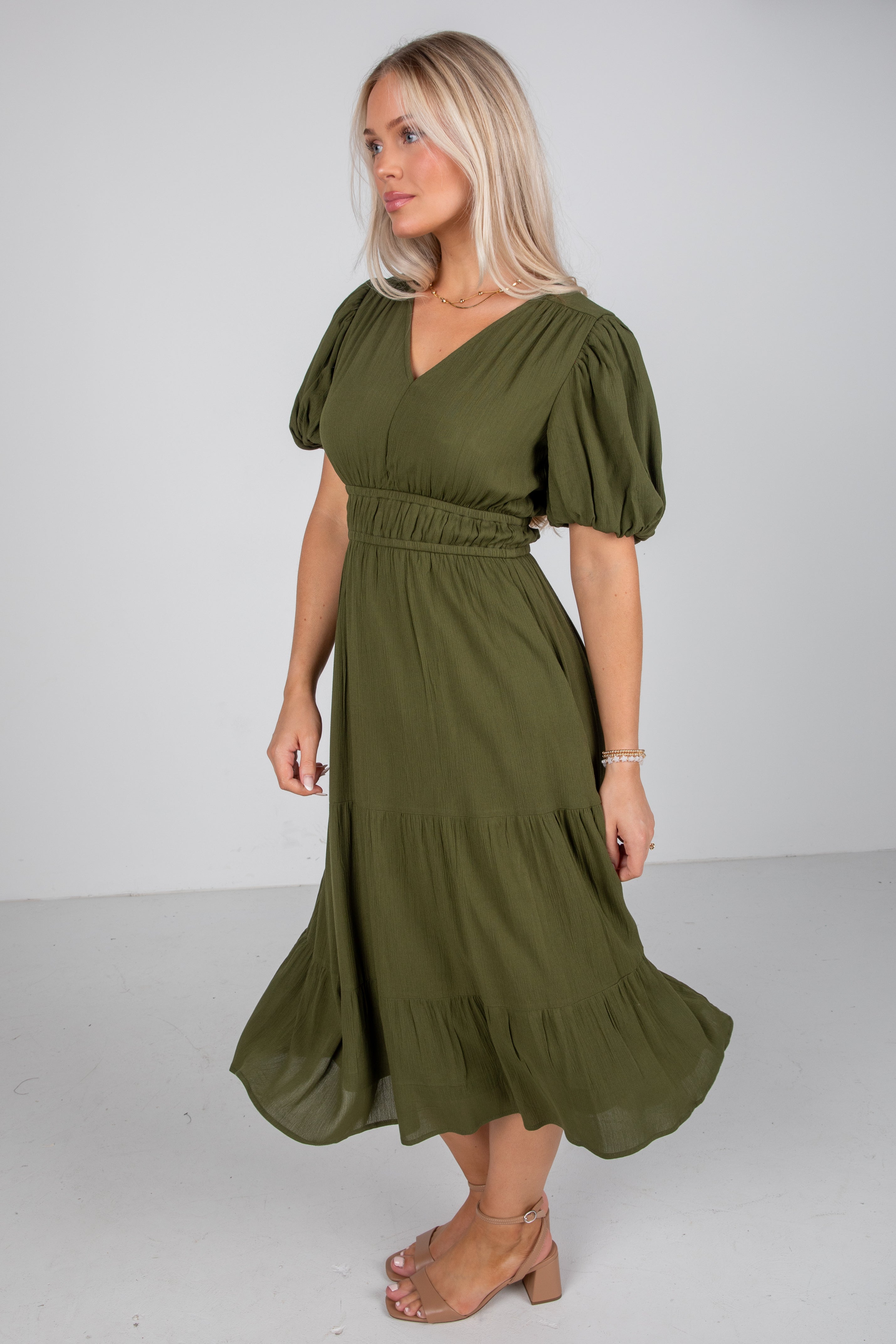 Woman wearing an olive green dress with puffed sleeves on a white background