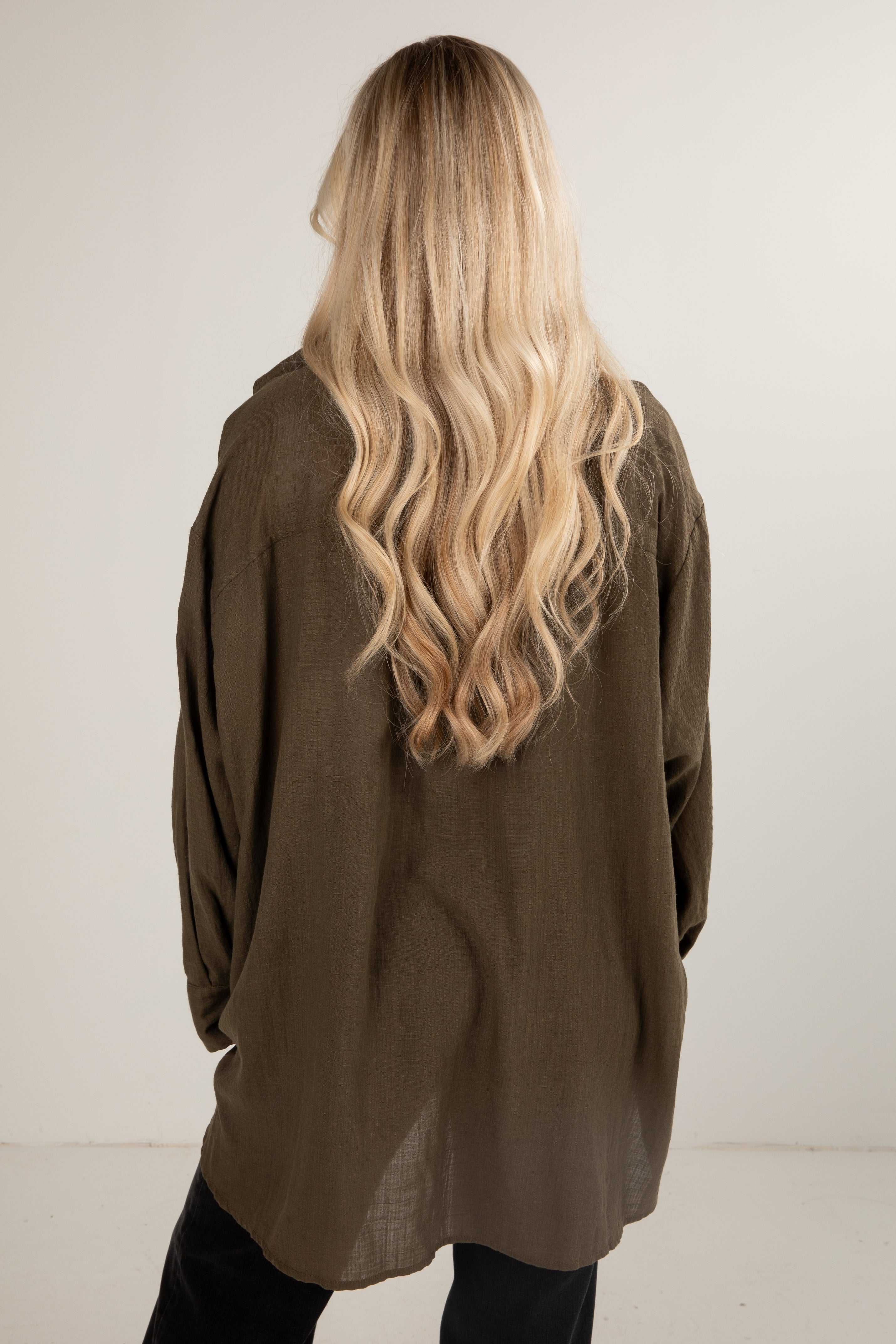 Person wearing an olive green jacket with long blonde hair, standing against a white background