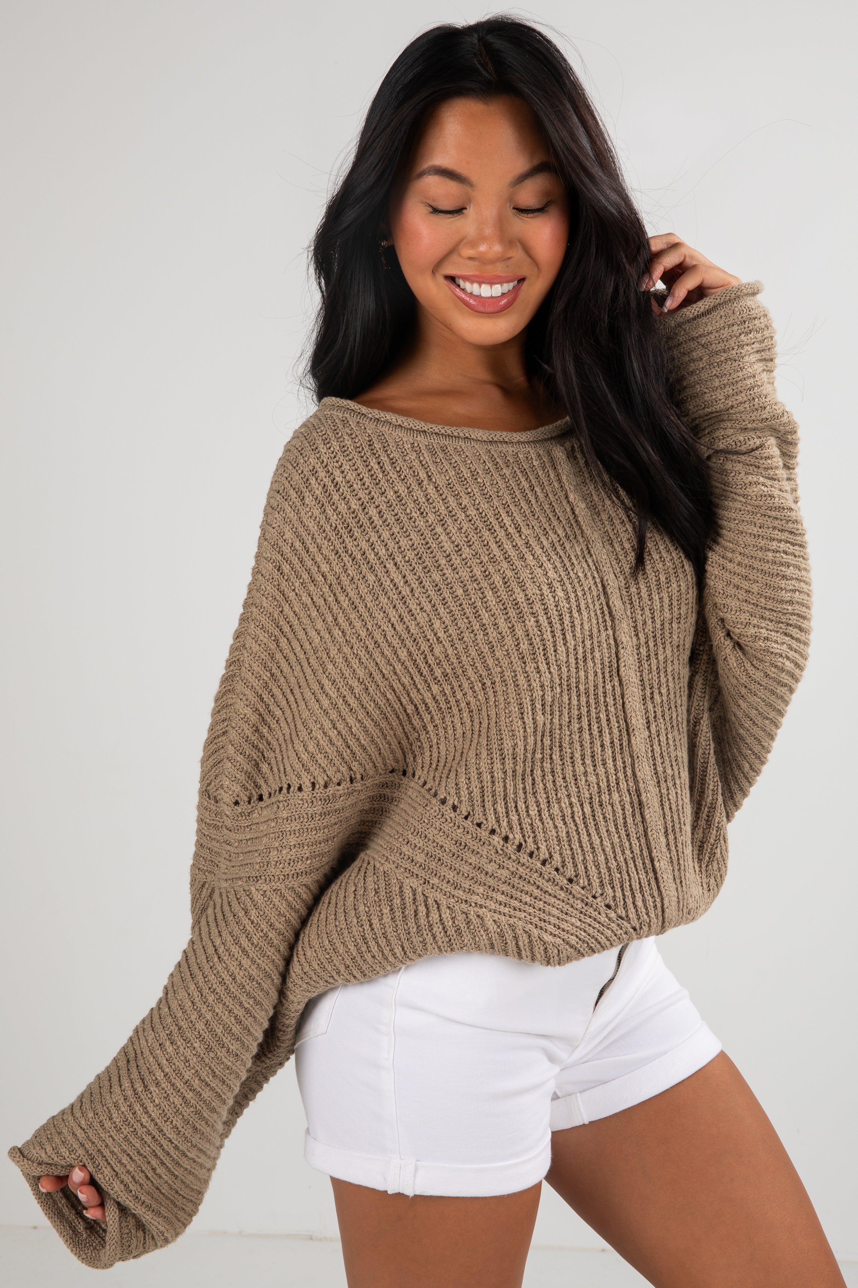 Woman wearing a brown sweater and white shorts against a plain background