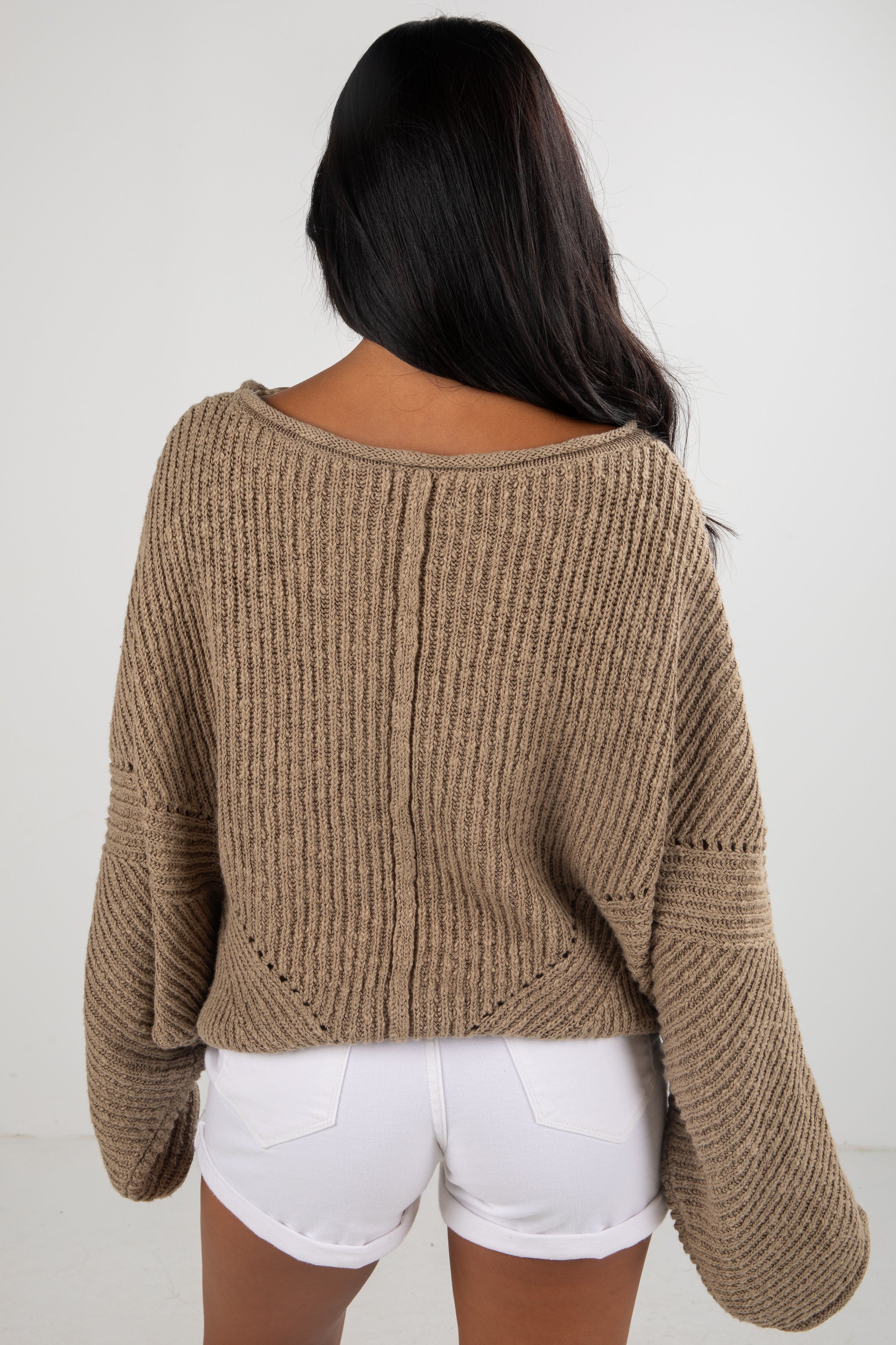Person wearing a brown knitted sweater and white shorts on a plain background