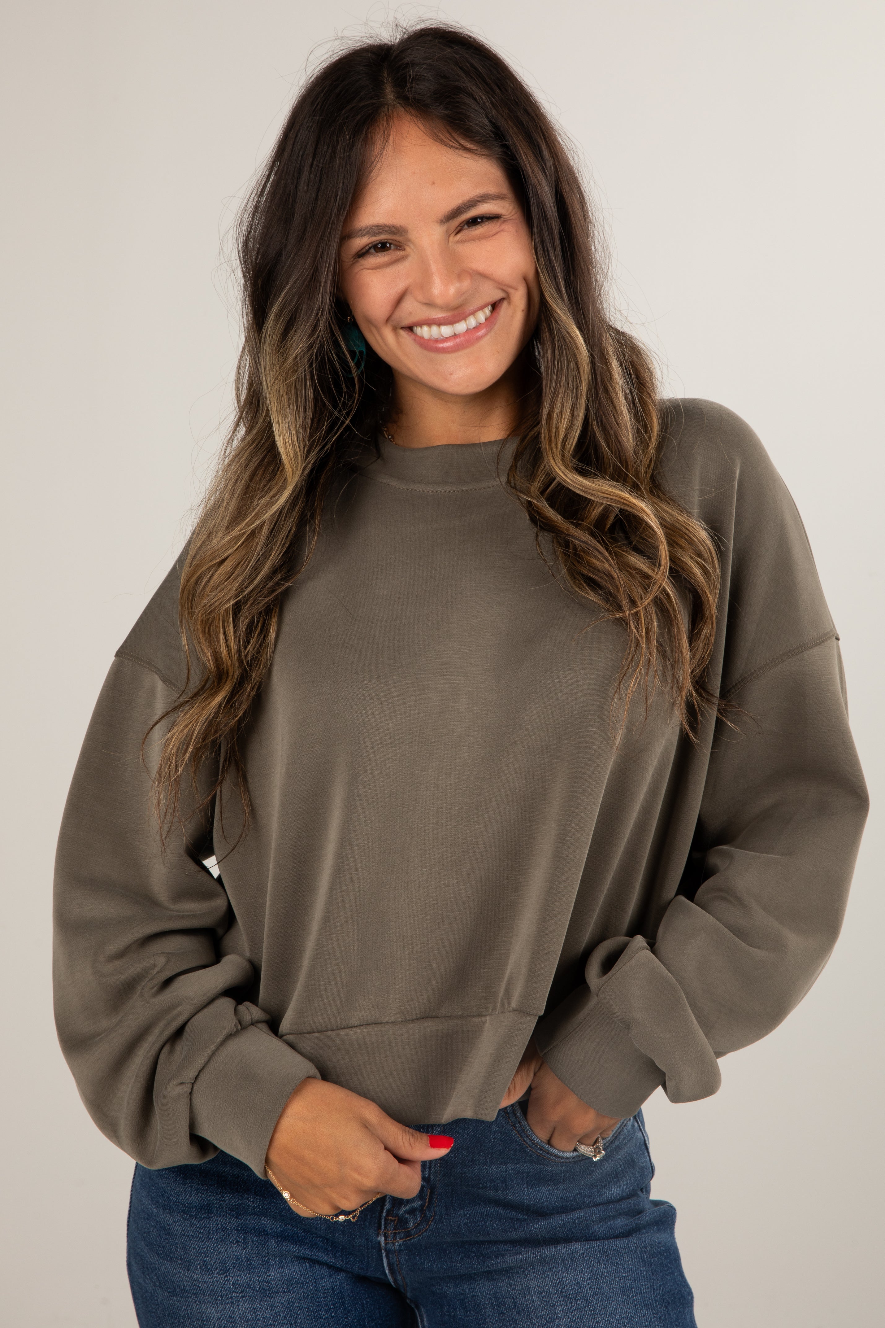 Woman wearing a brown sweatshirt and blue jeans against a plain background