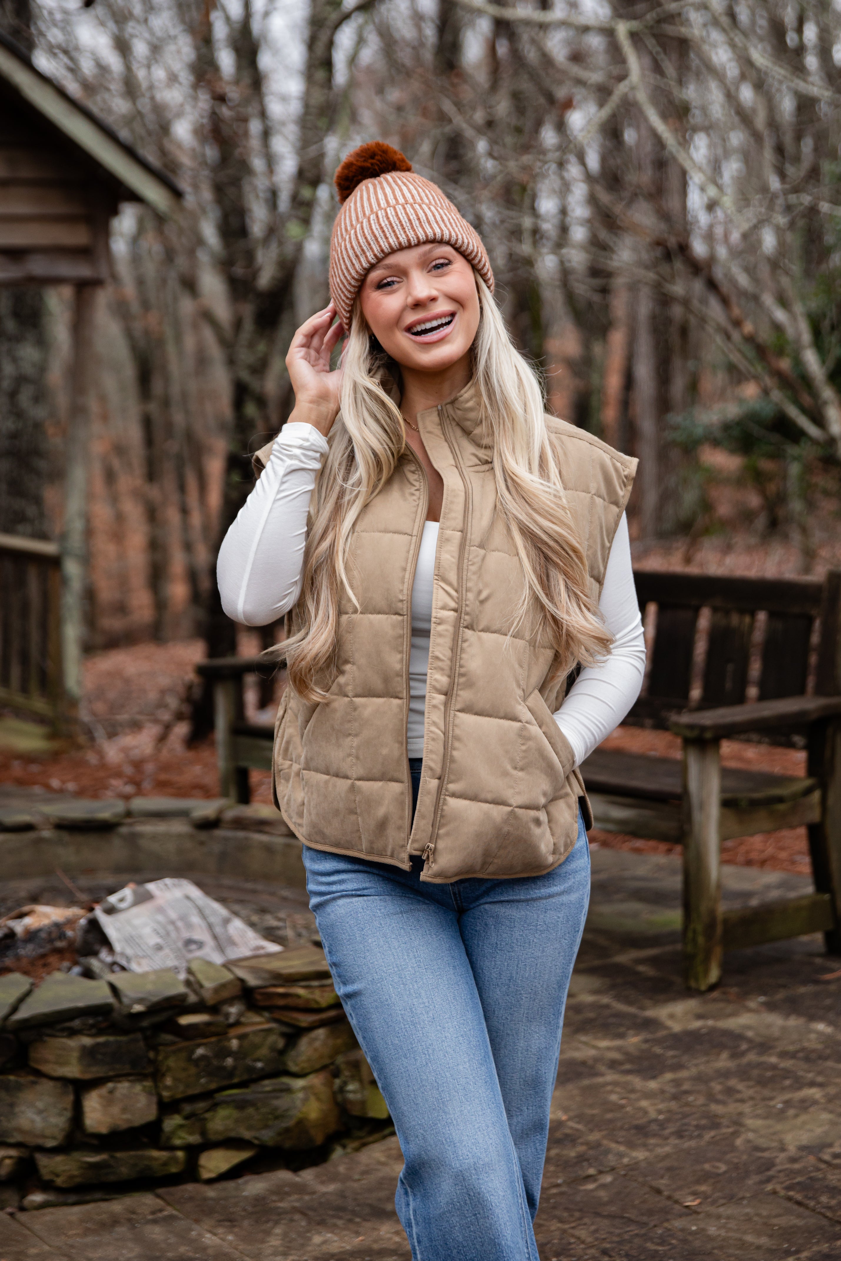 Woman wearing a beige puffer vest and knit hat in a forest setting