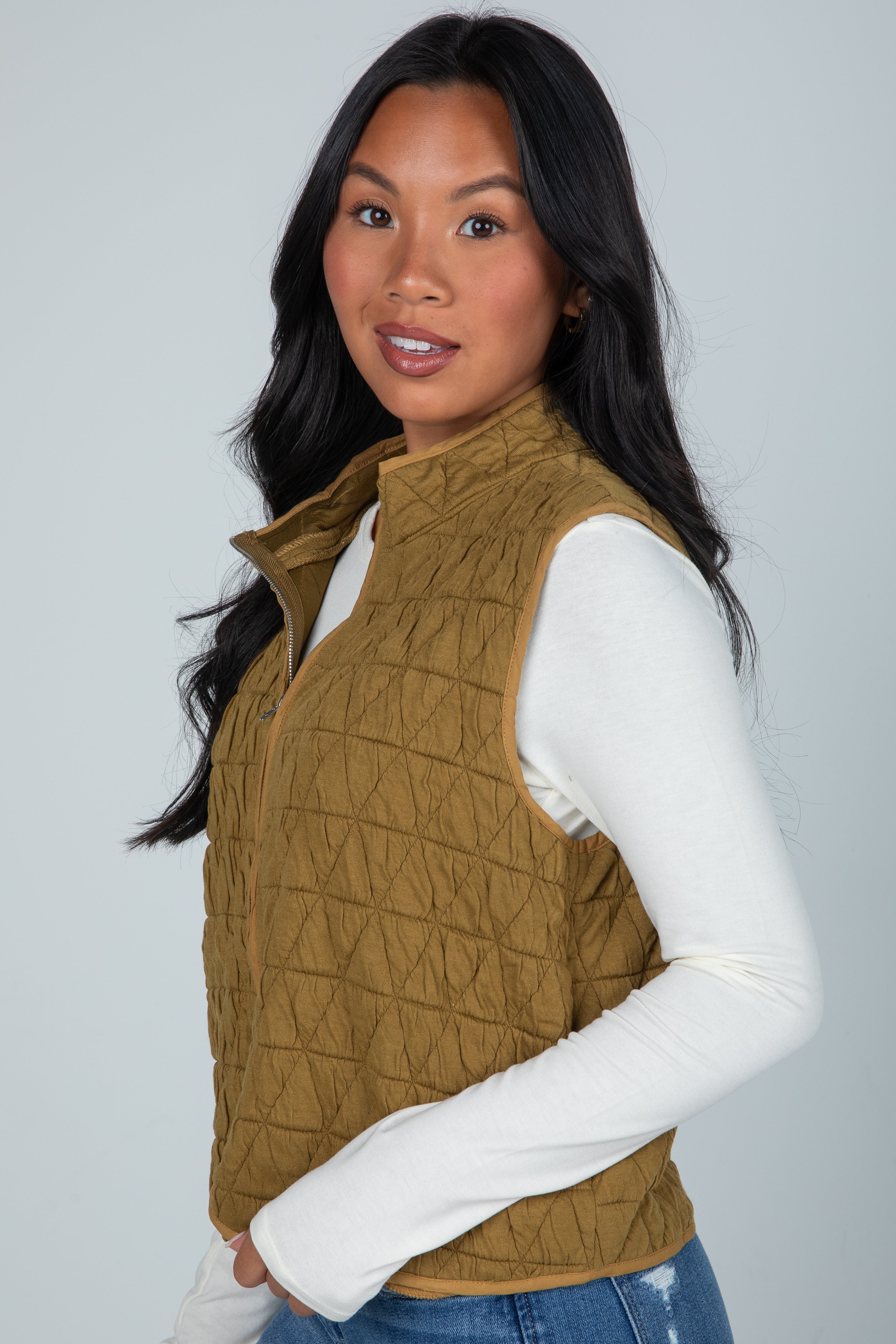 Woman wearing a quilted brown vest over a white long-sleeve shirt on a gray background