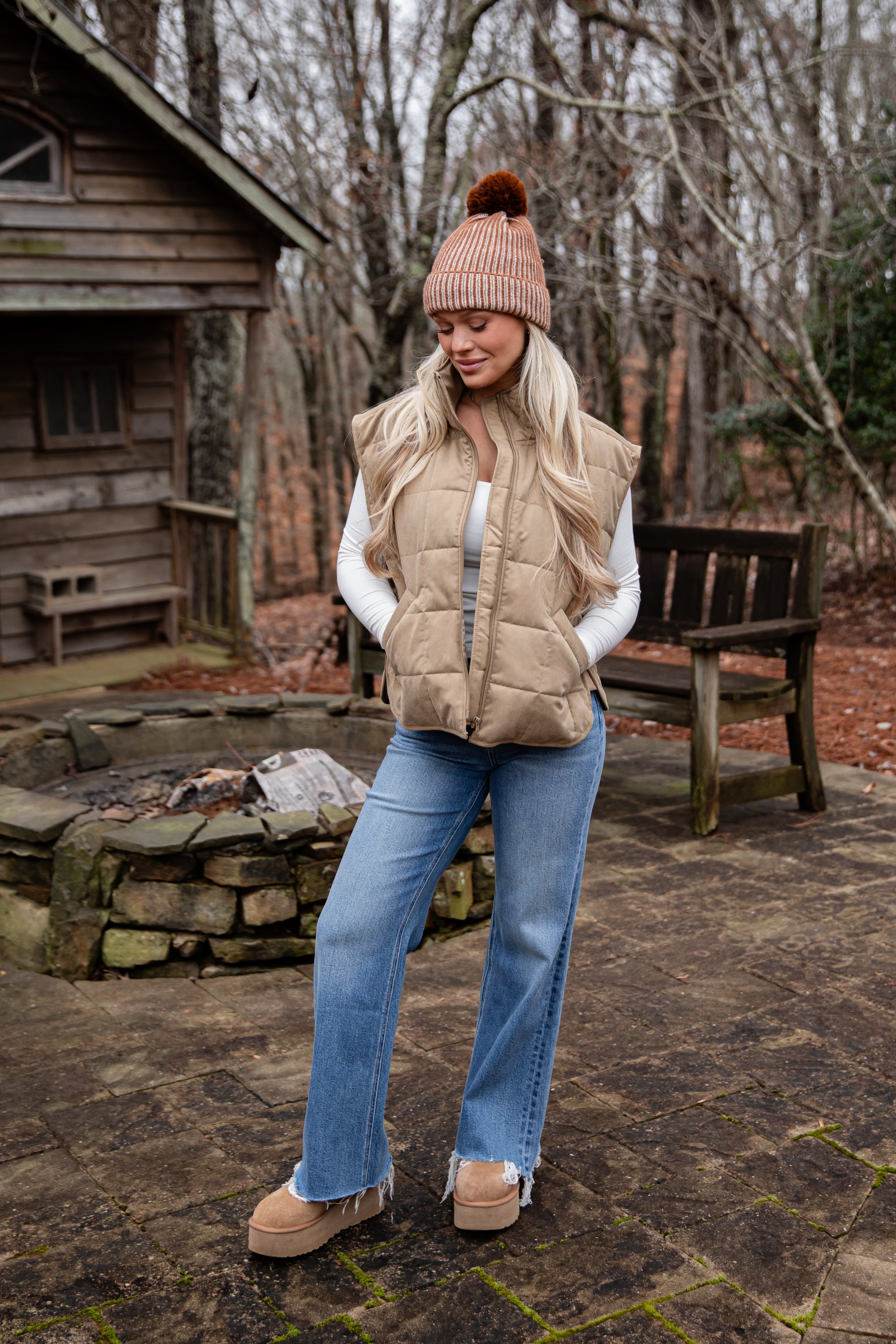 Woman in winter clothing standing outdoors near a wooden cabin.
