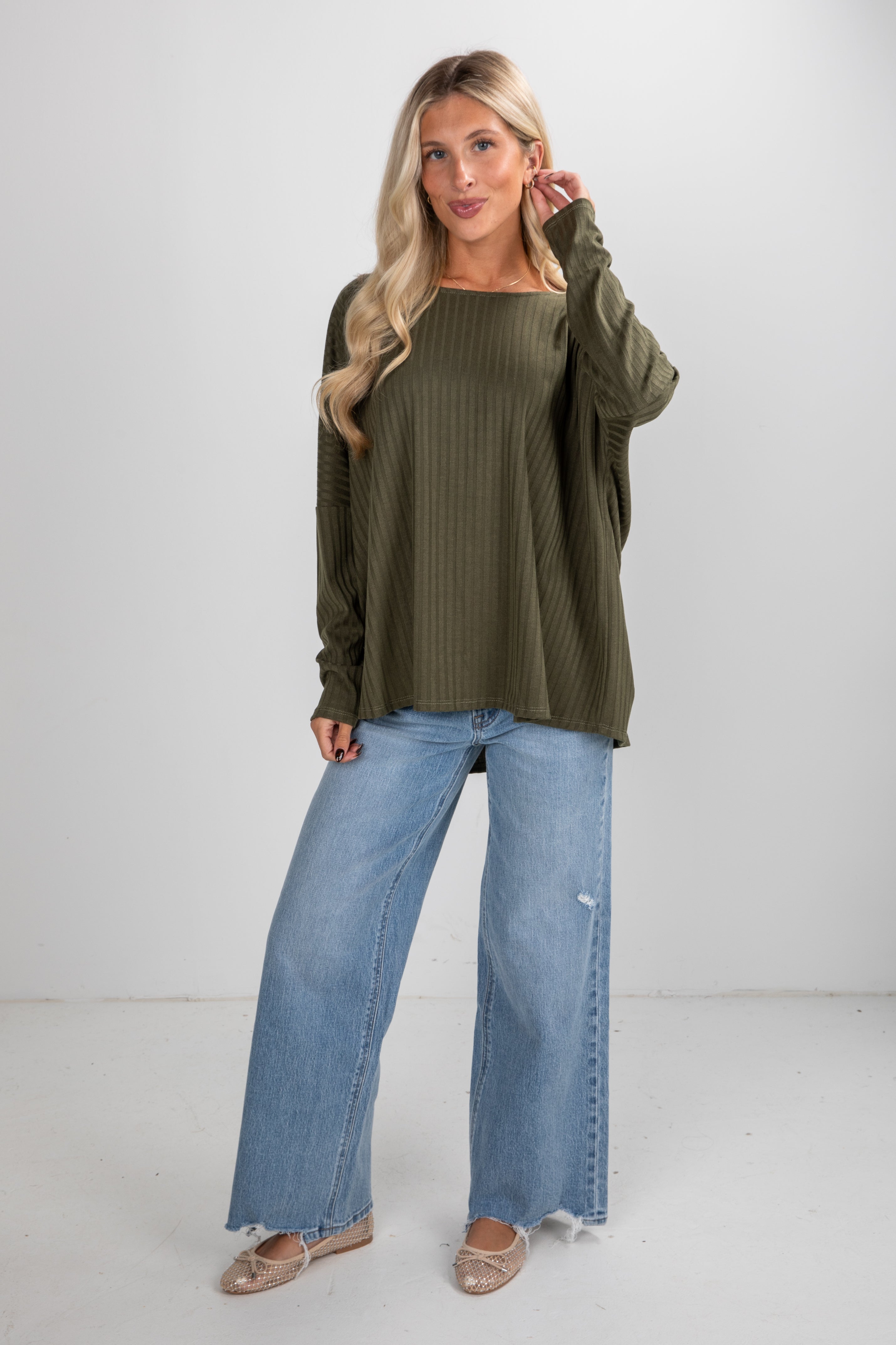 Woman wearing an olive green sweater and blue jeans on a white background