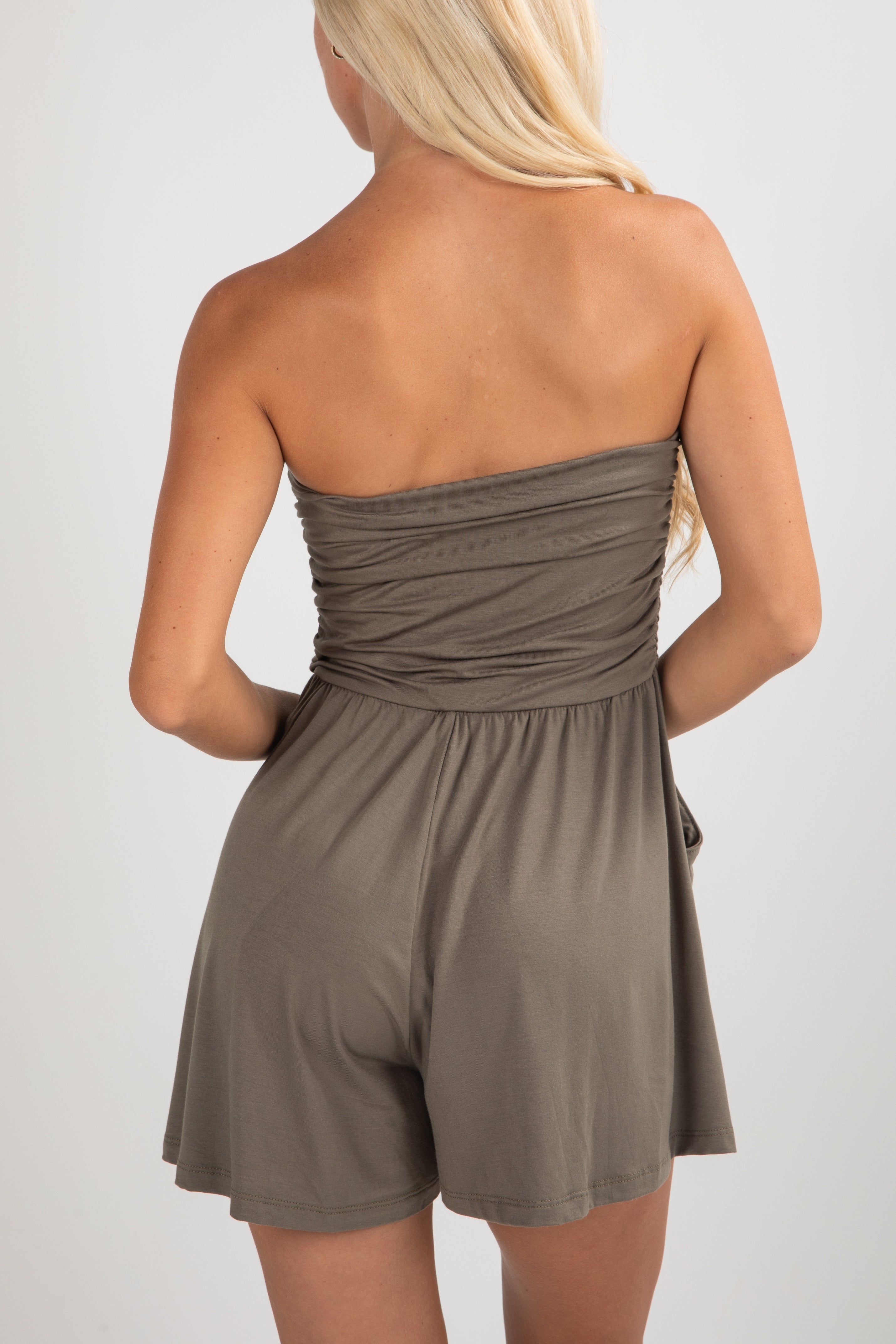 Woman wearing a strapless brown romper on a plain background