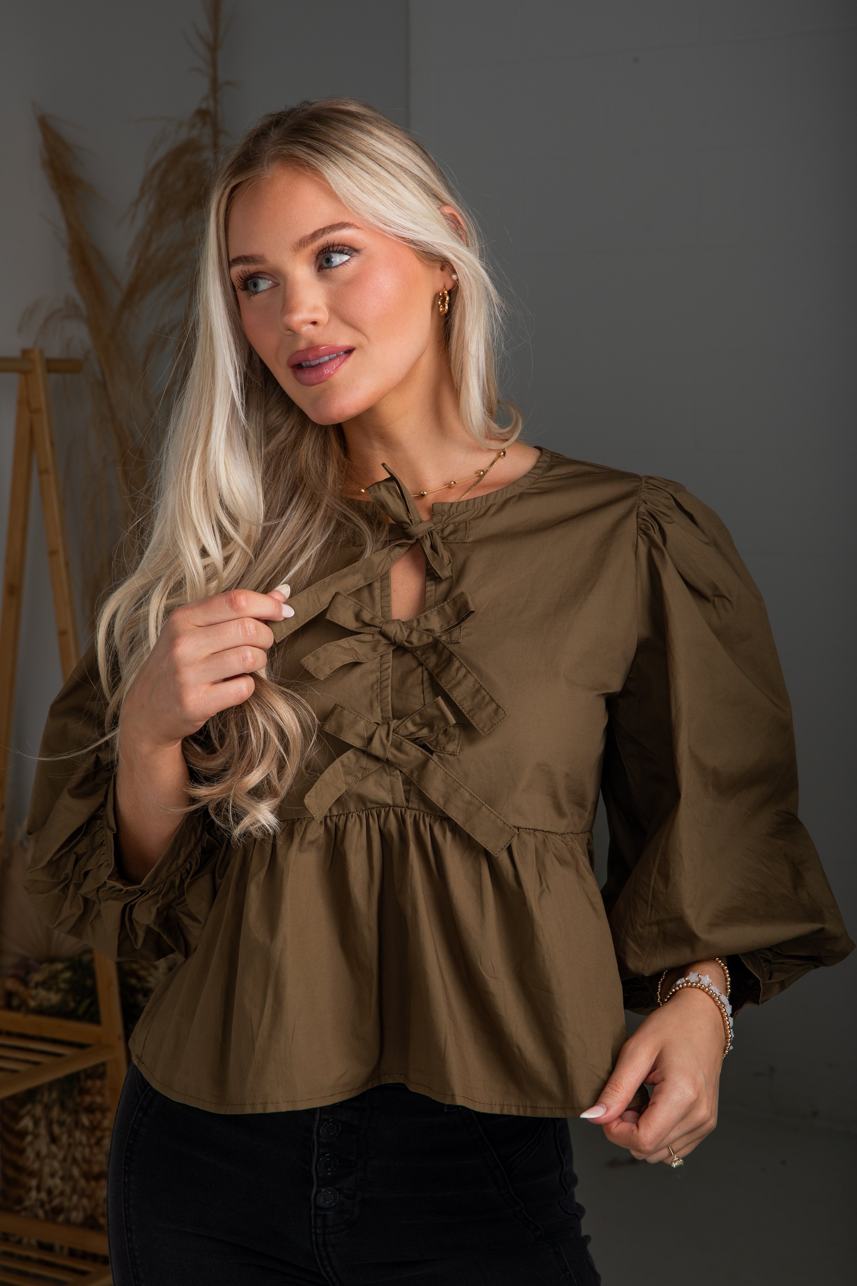 Woman wearing a brown blouse with ruffled details against a neutral background