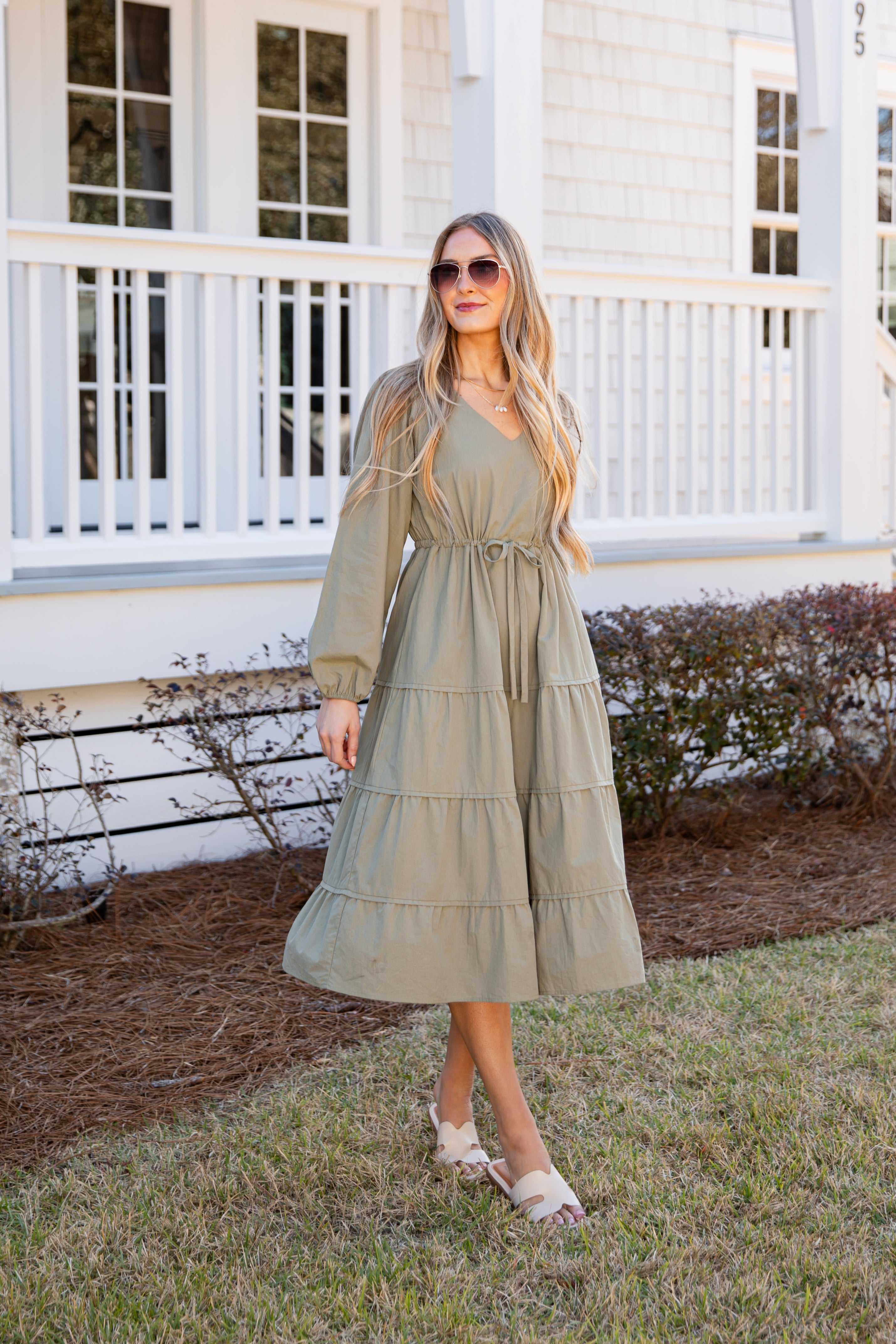 Woman in a green dress standing in front of a white house with a porch.