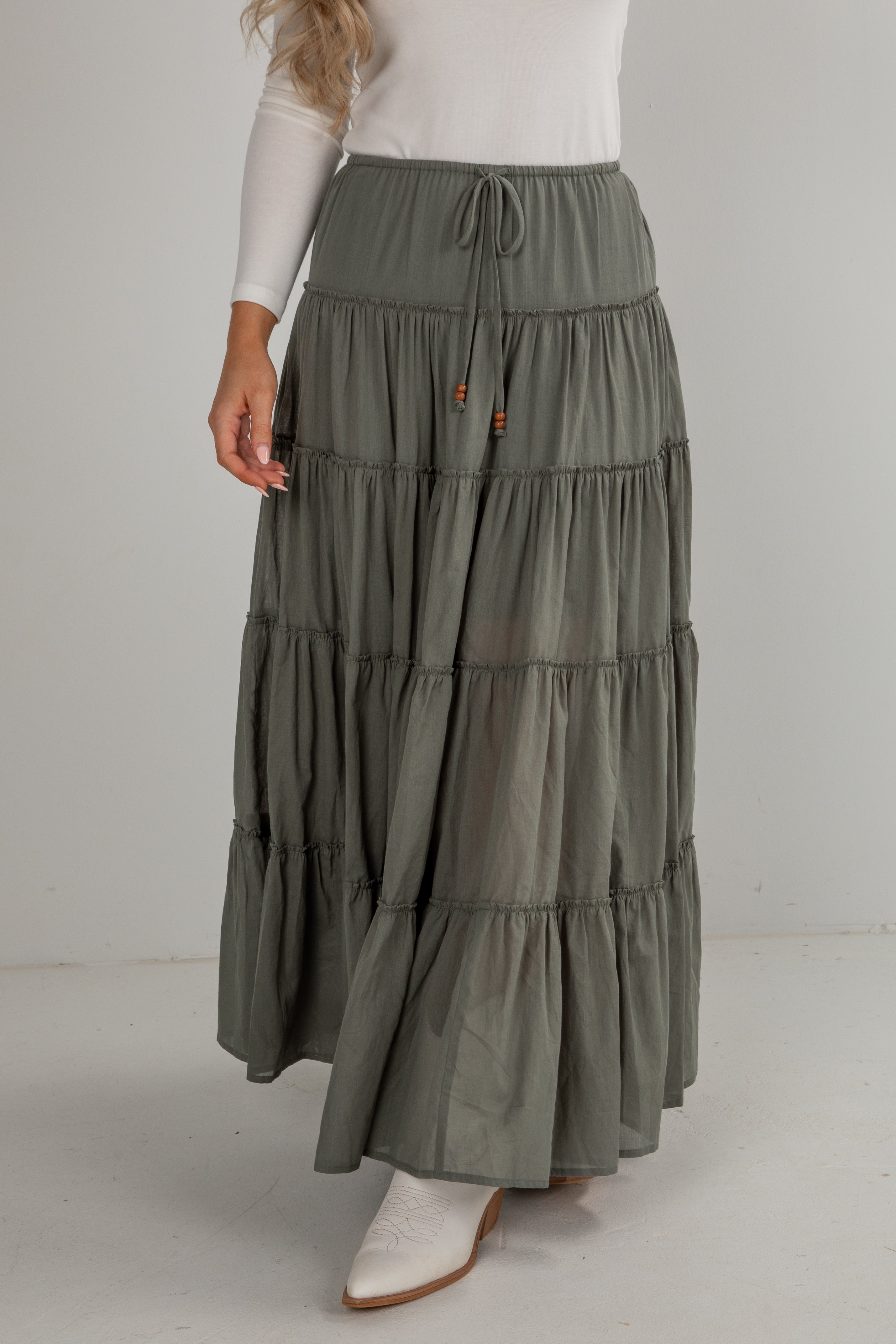 Woman wearing a long, tiered olive green skirt on a white background