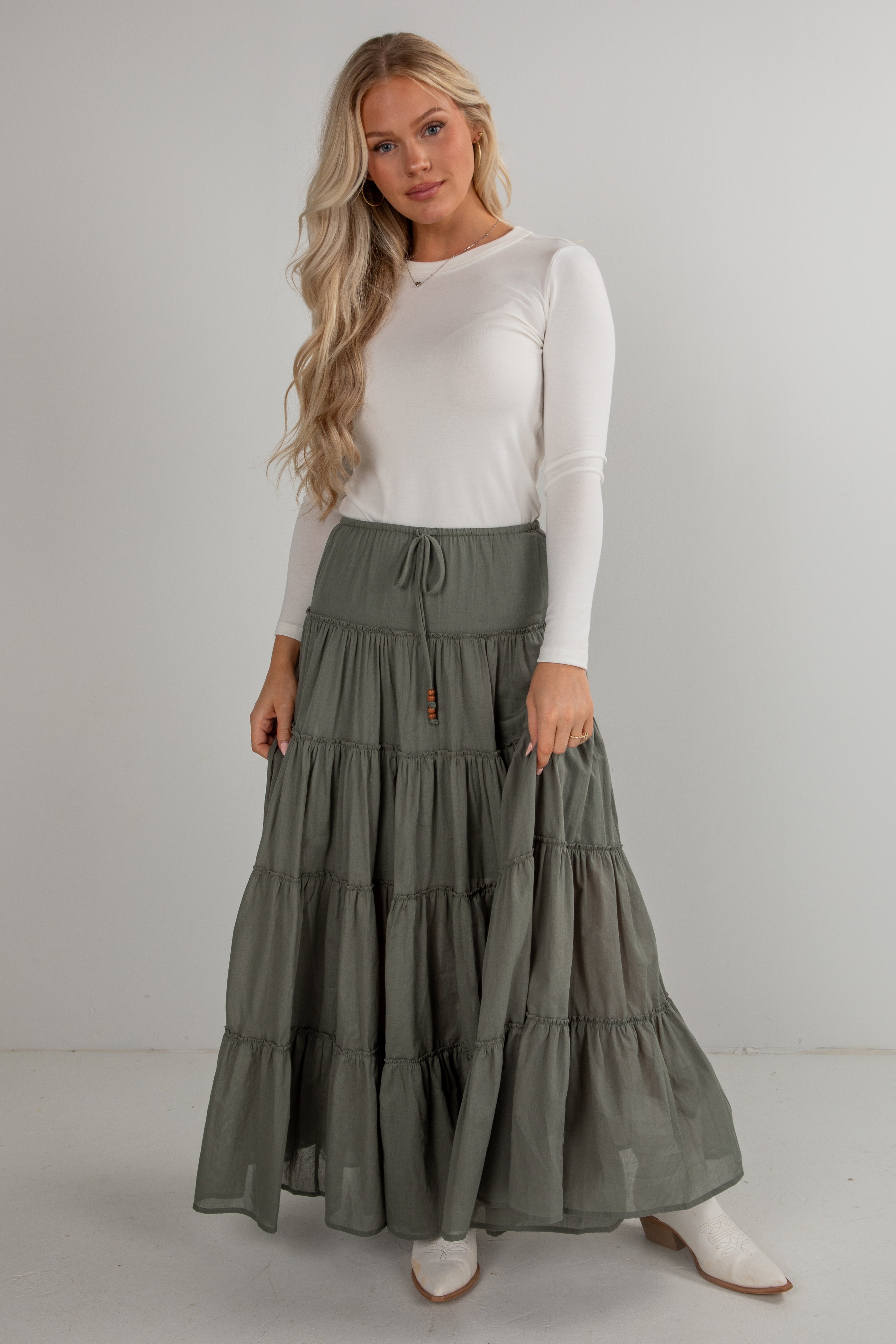 Woman wearing a white long-sleeve top and green tiered skirt on a plain background