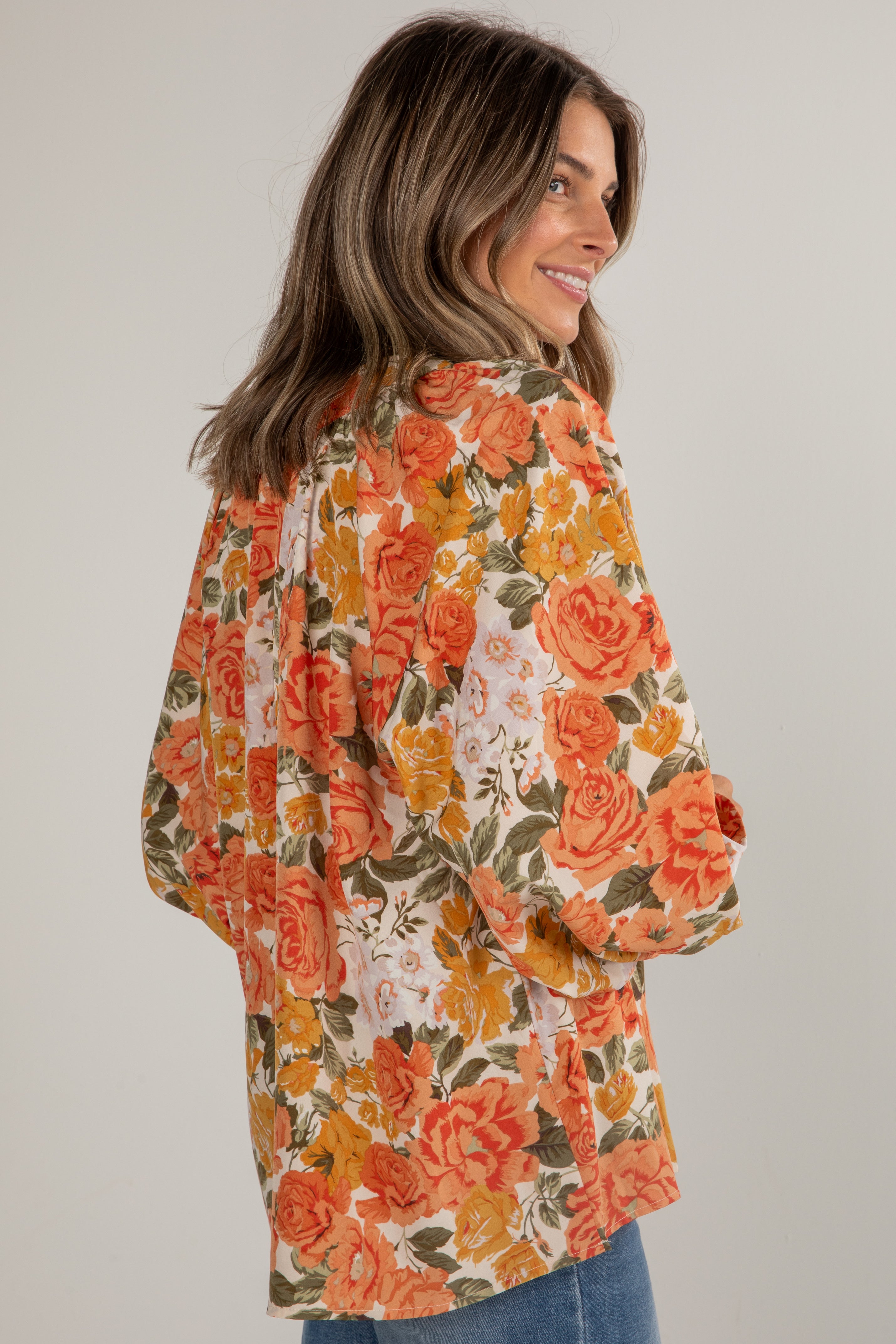 Woman wearing a floral blouse with orange and yellow flowers on a plain background