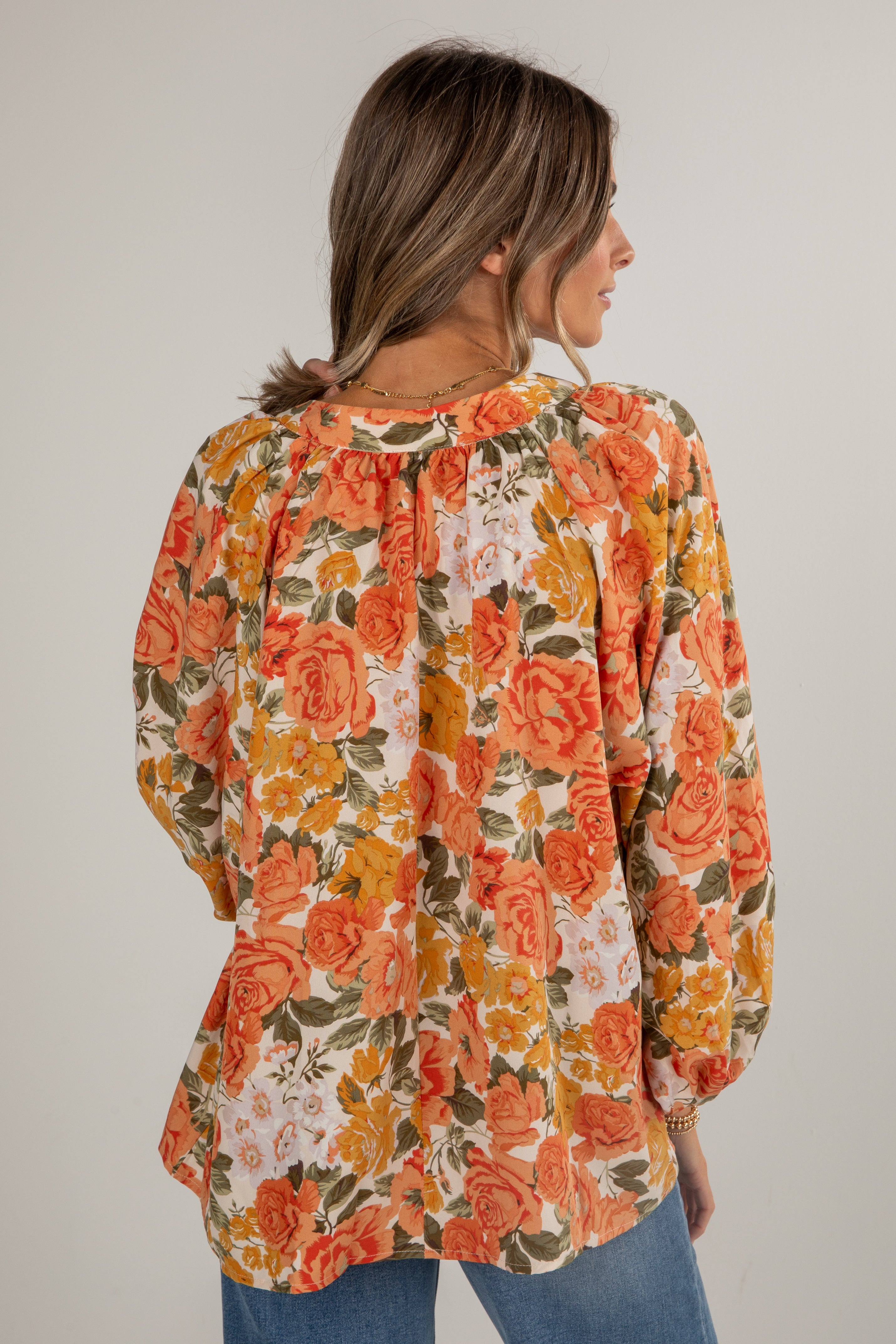Woman wearing a floral blouse with orange and yellow flowers on a plain background