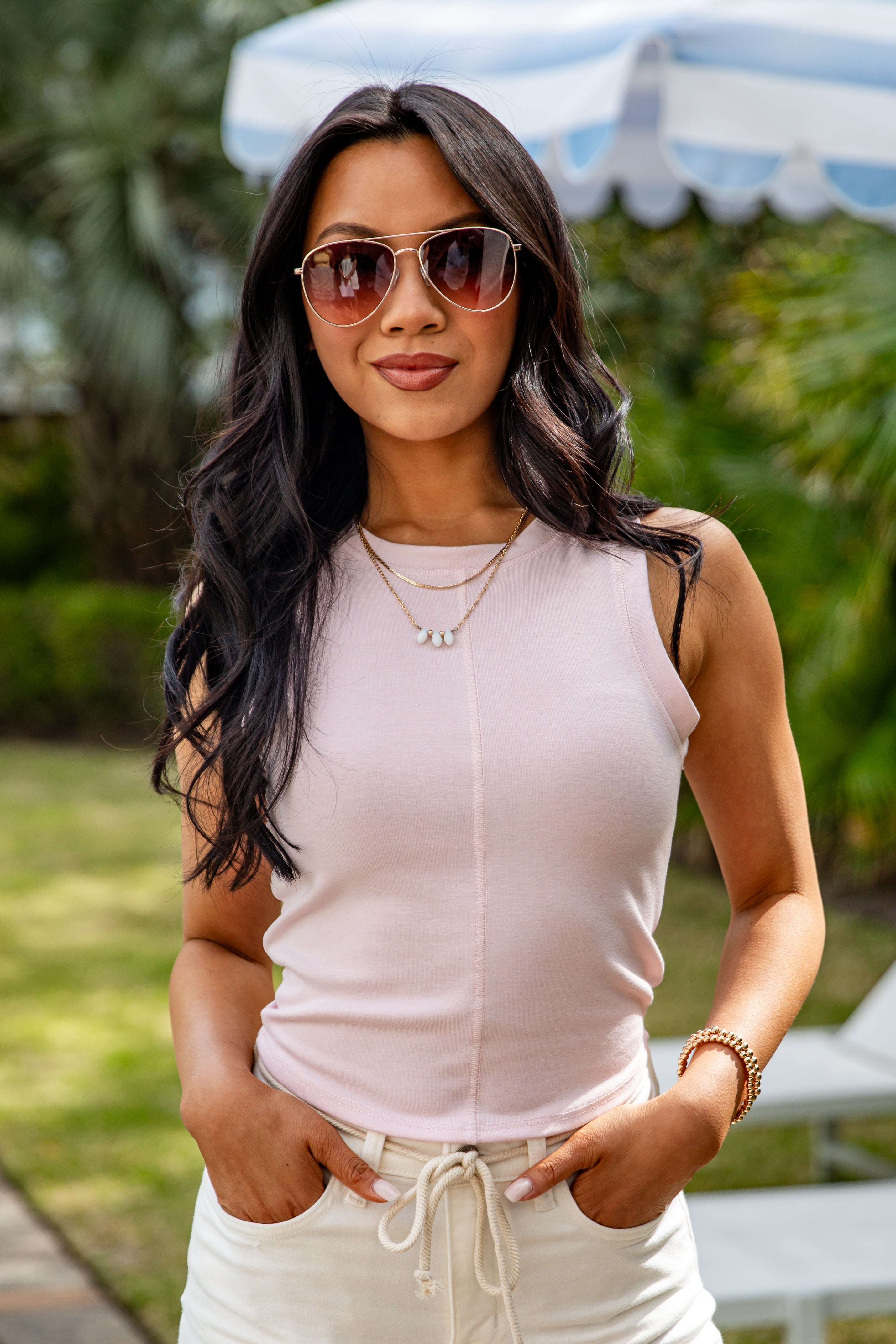 Woman wearing sunglasses and a light pink sleeveless top outdoors