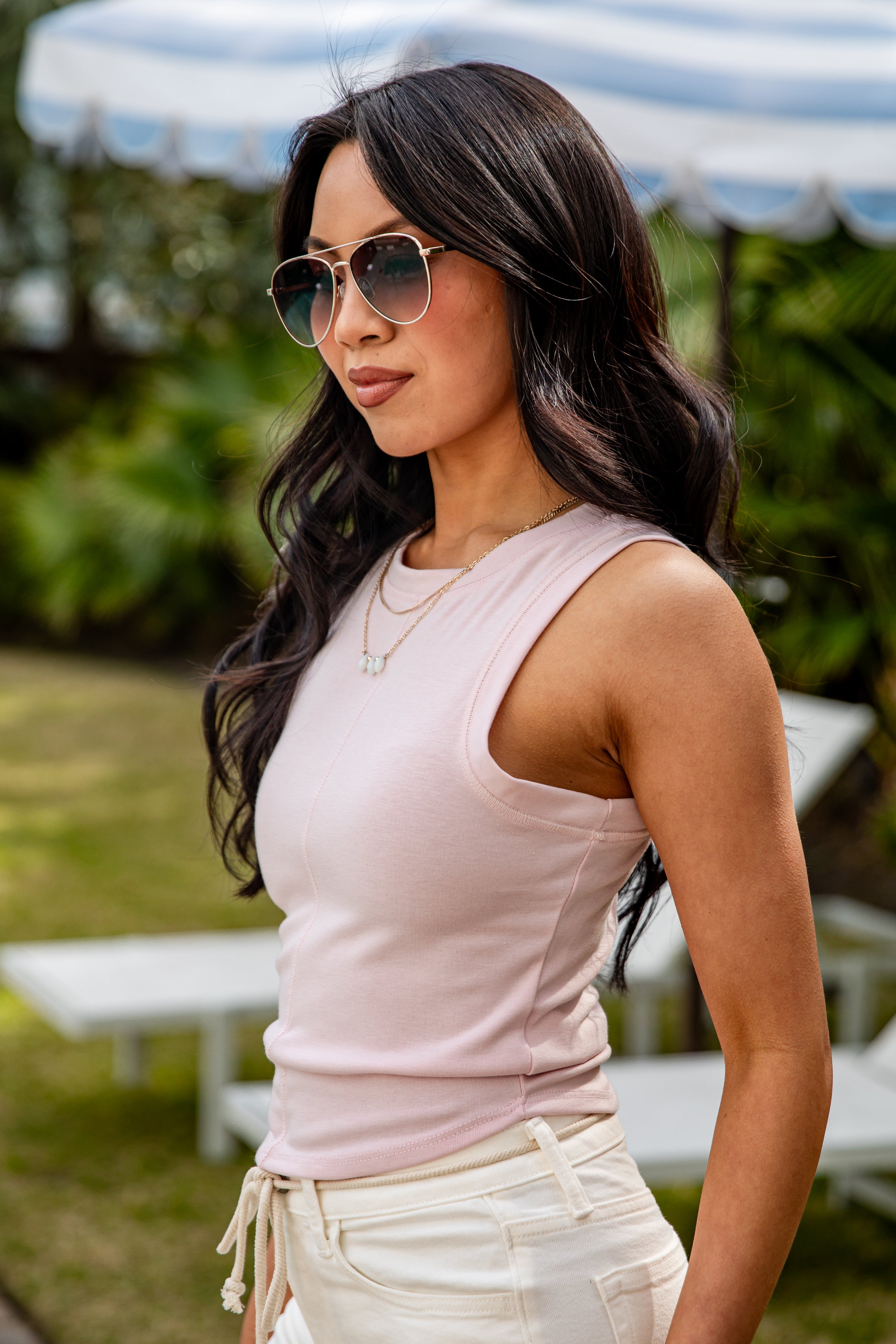 Woman wearing a light pink sleeveless top and sunglasses outdoors