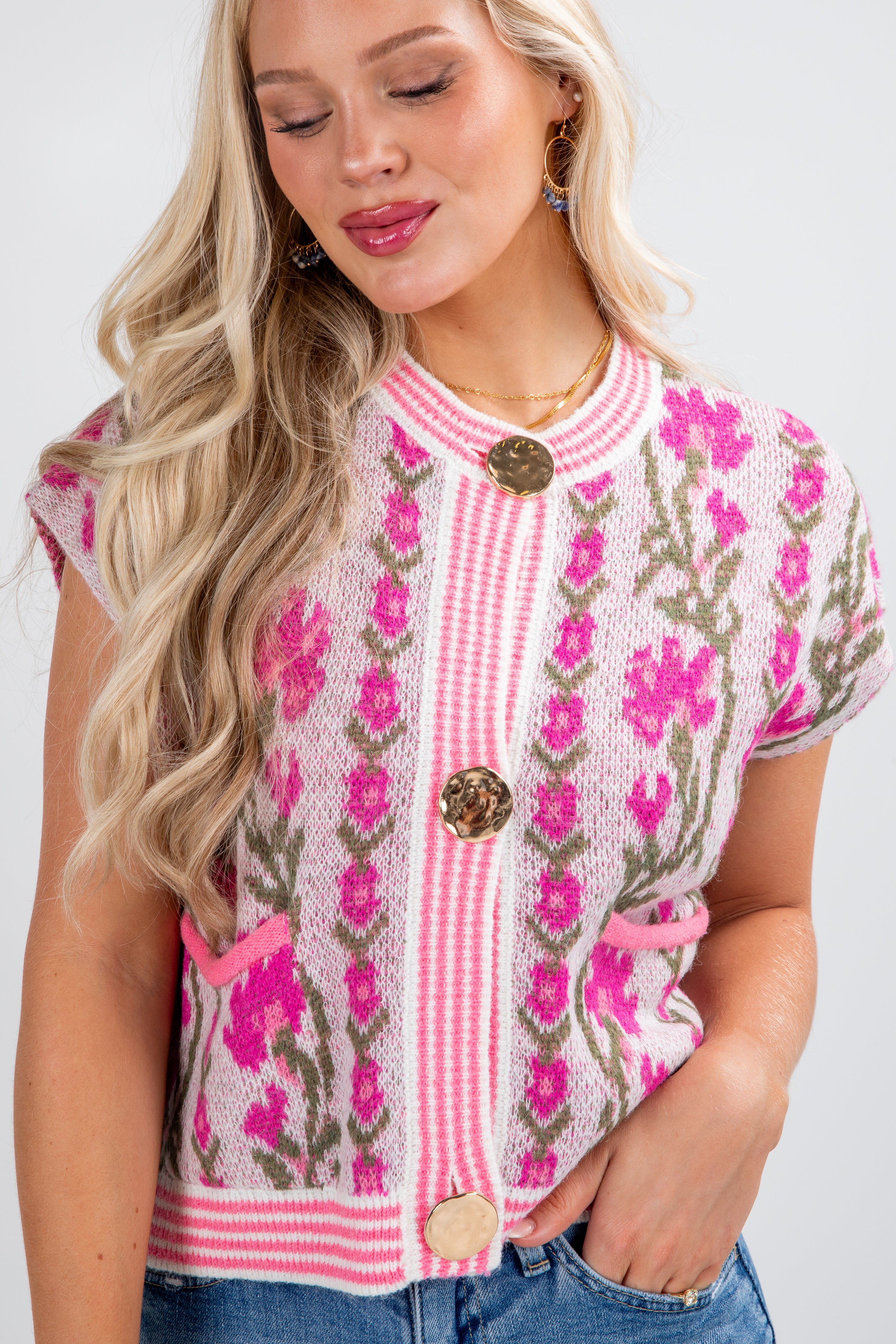 Woman wearing a pink floral embroidered top with buttons on a white background