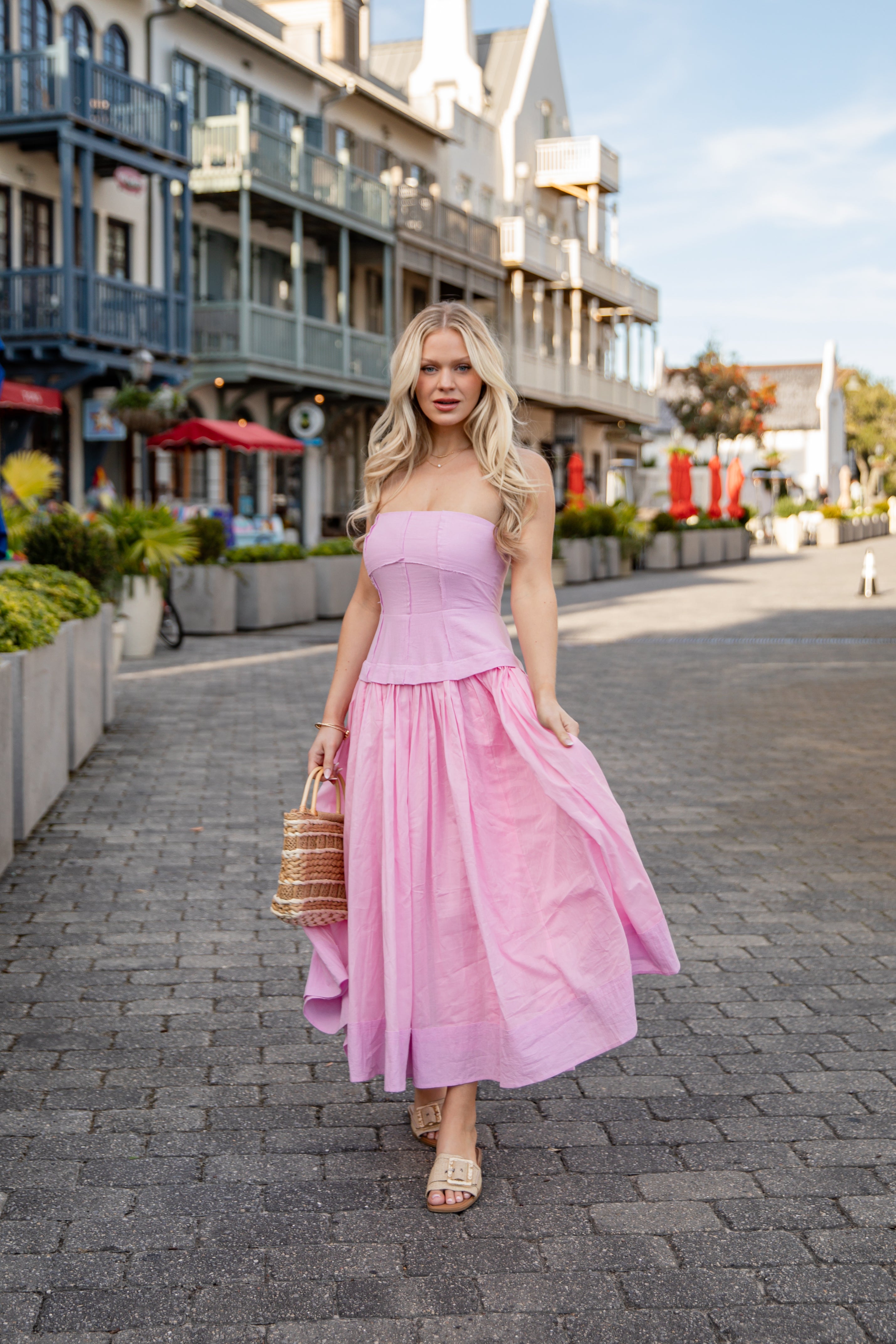 Woman in a pink dress walking on a street with shops in the background