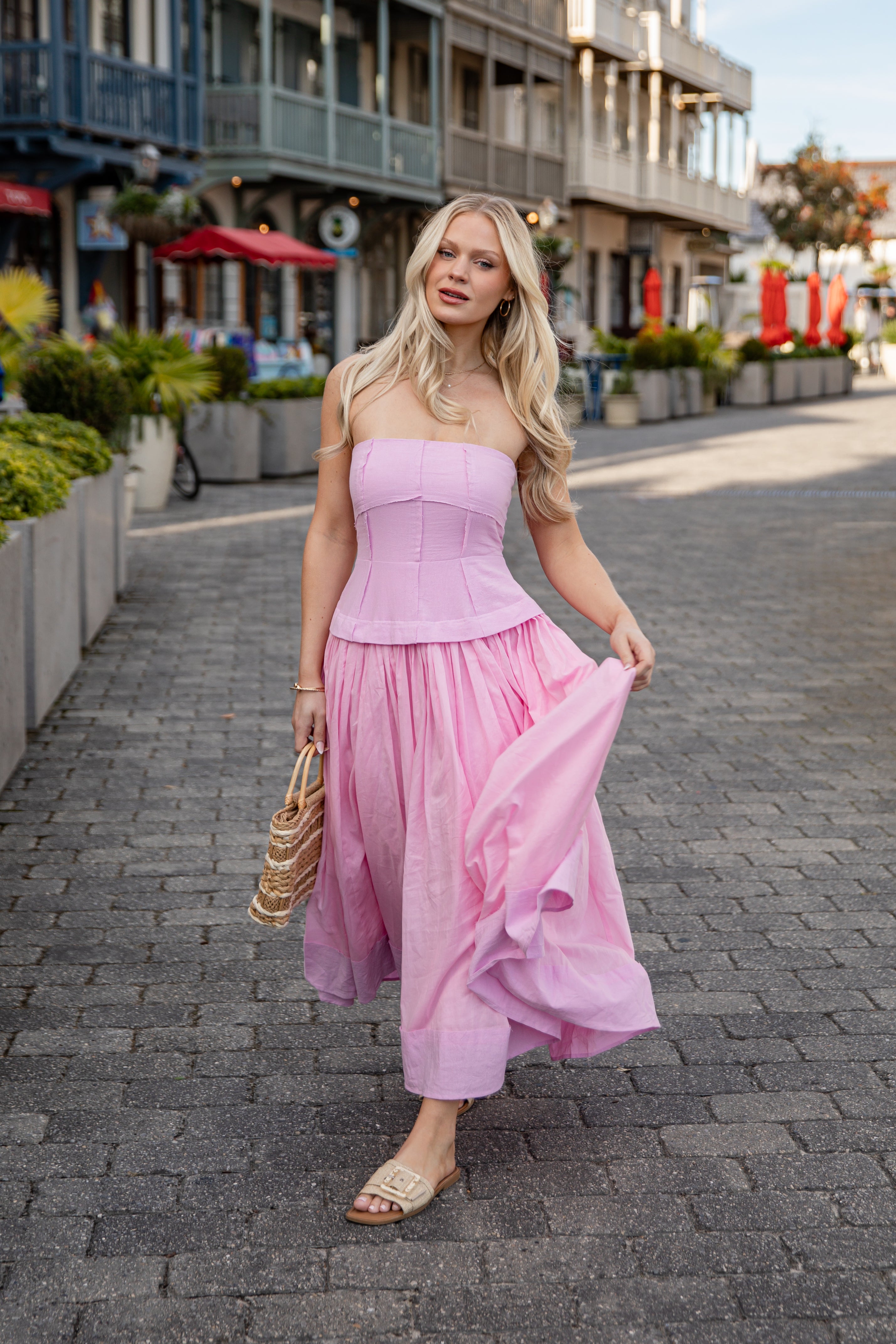 Woman in a pink strapless dress walking on a street with shops in the background