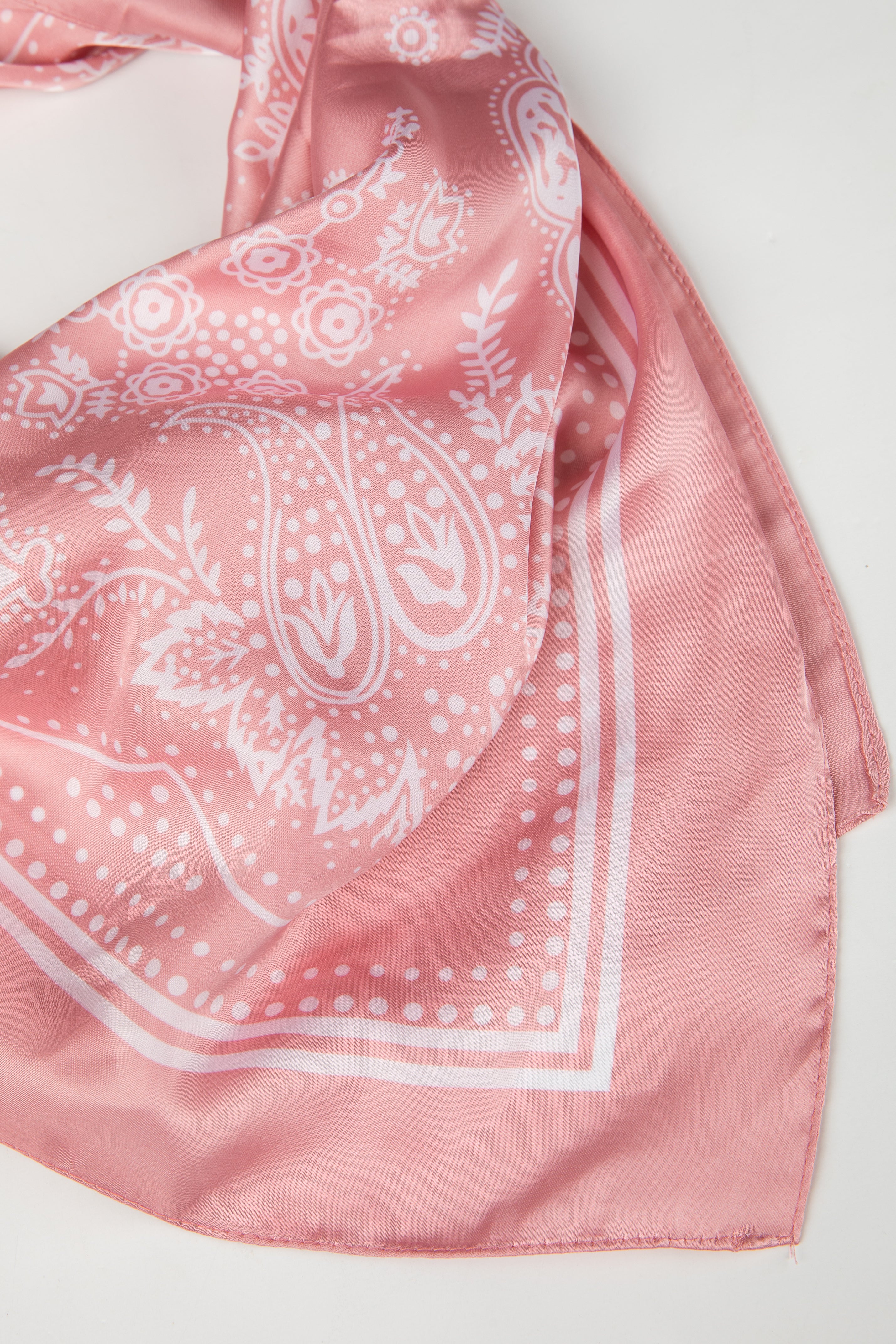 Pink bandana with white paisley pattern on a light gray background