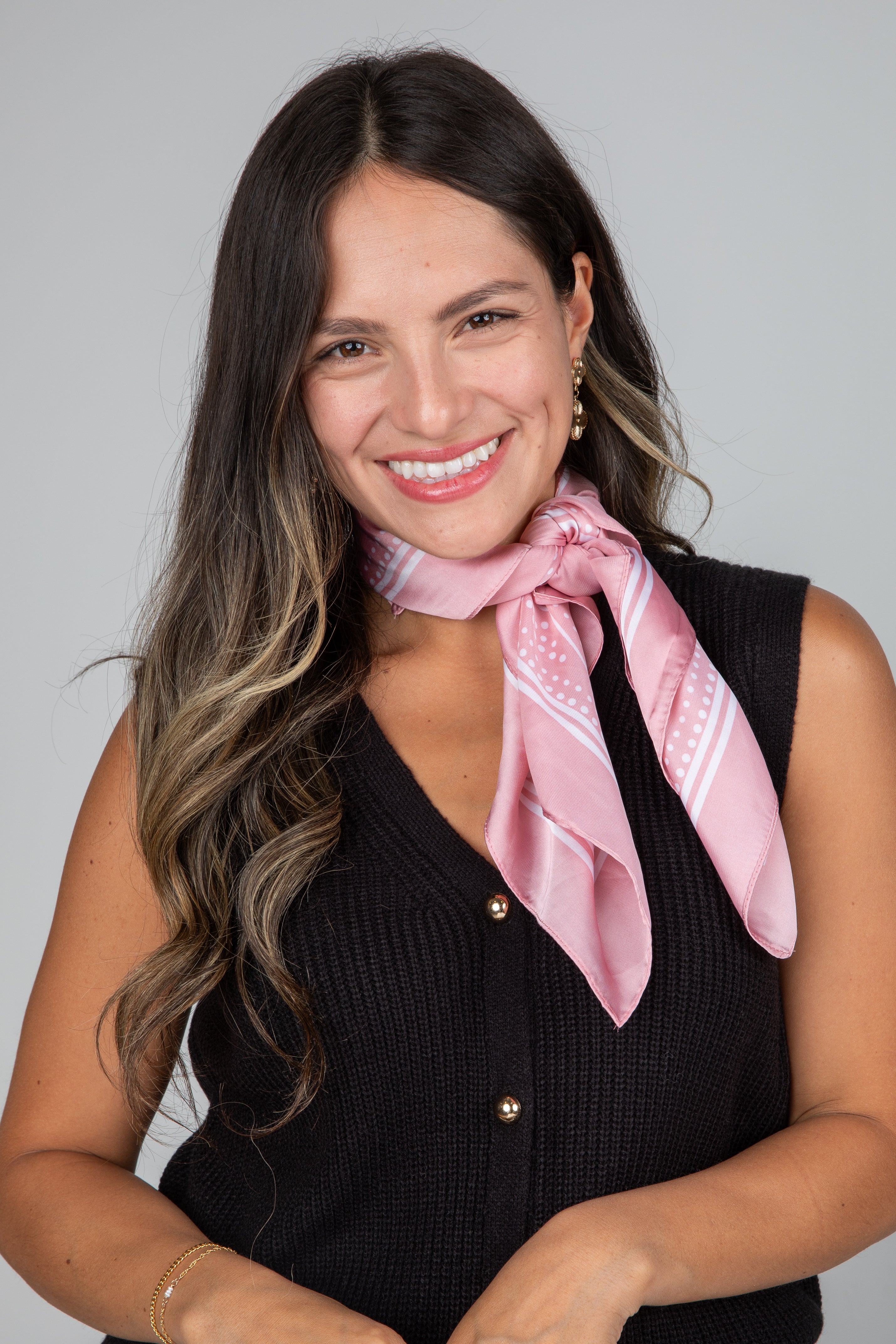 Woman wearing a pink scarf and black sleeveless top against a gray background