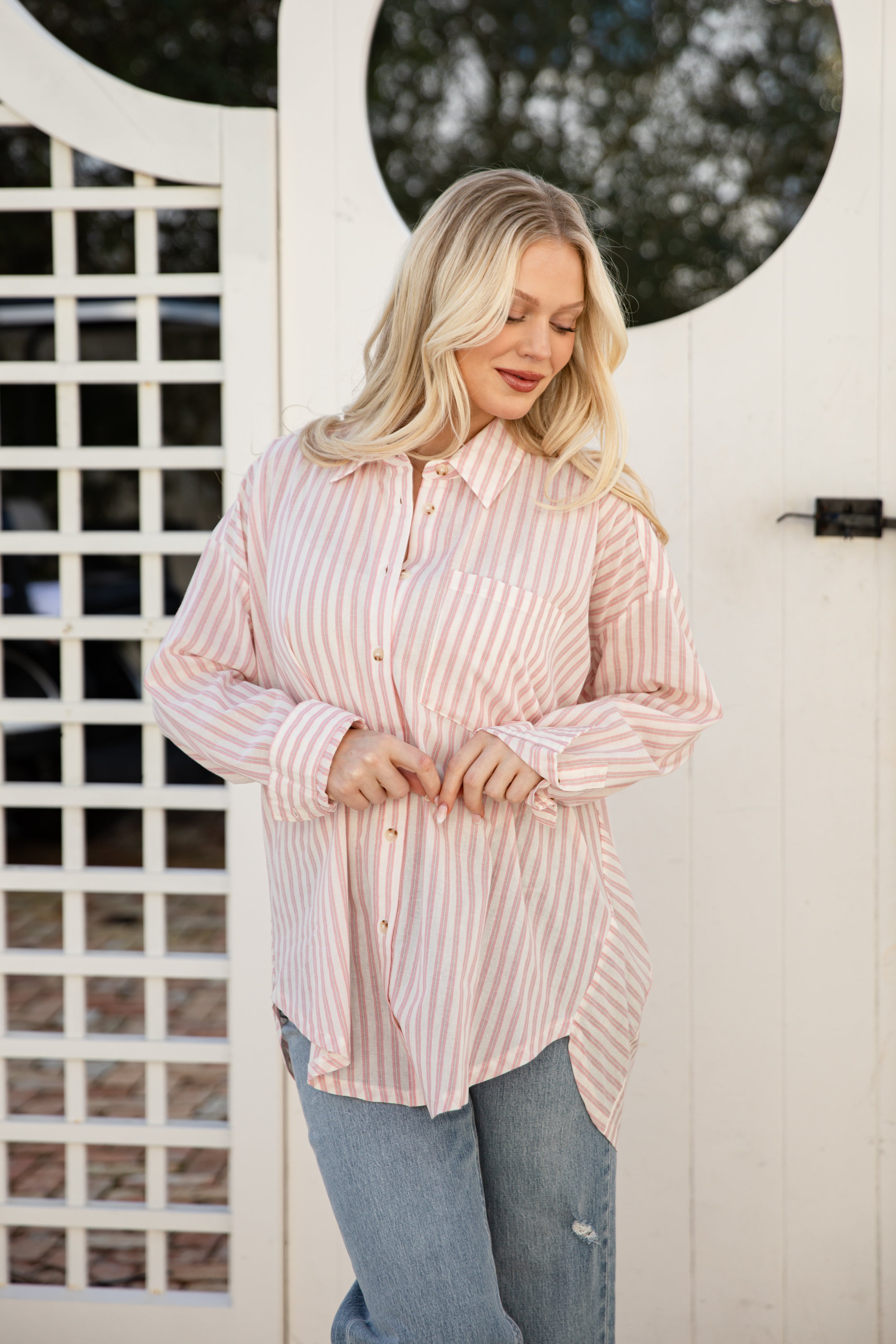 Woman wearing a pink and white striped shirt in front of a white door with circular window