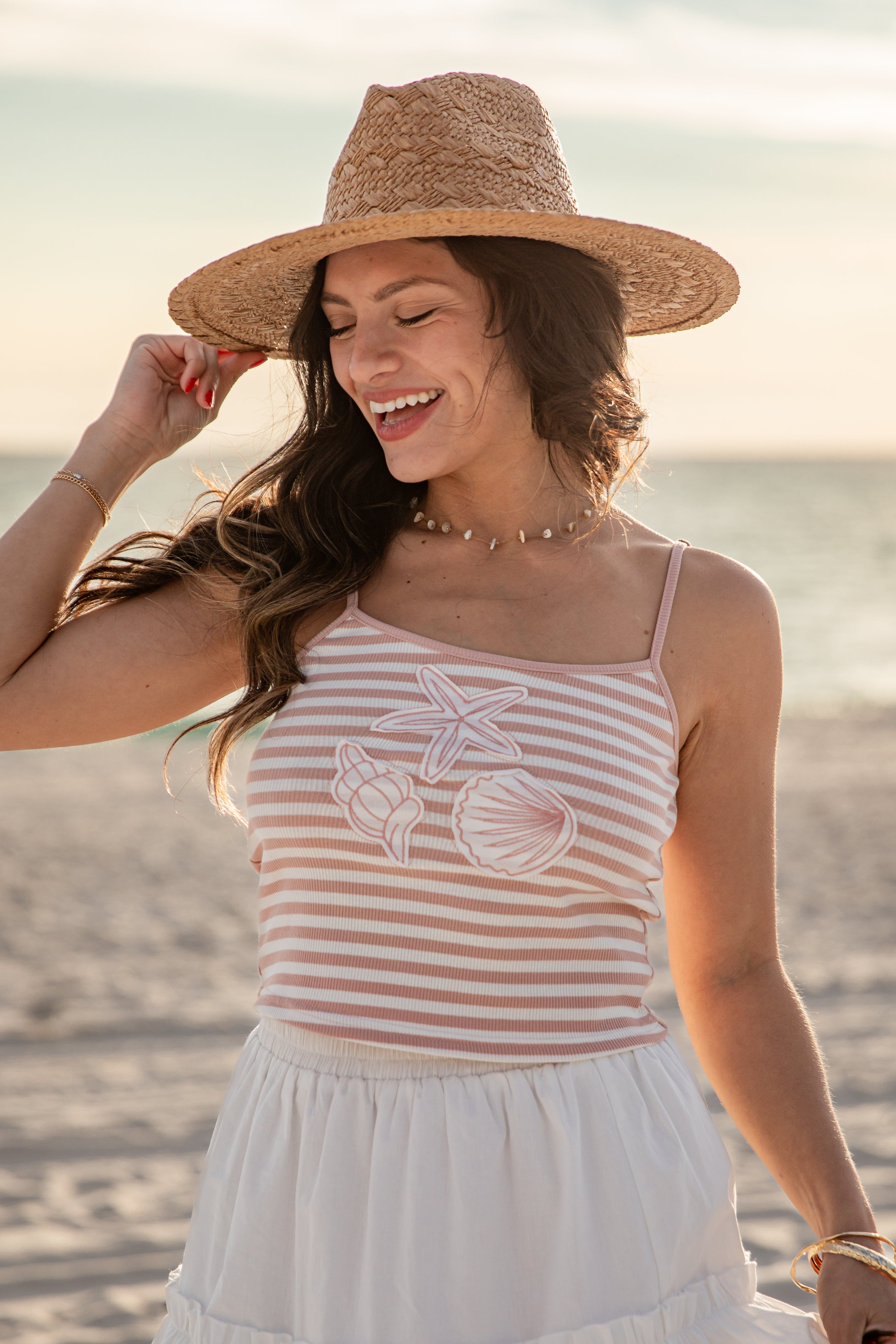 Woman on a beach wearing a striped tank top and straw hat.