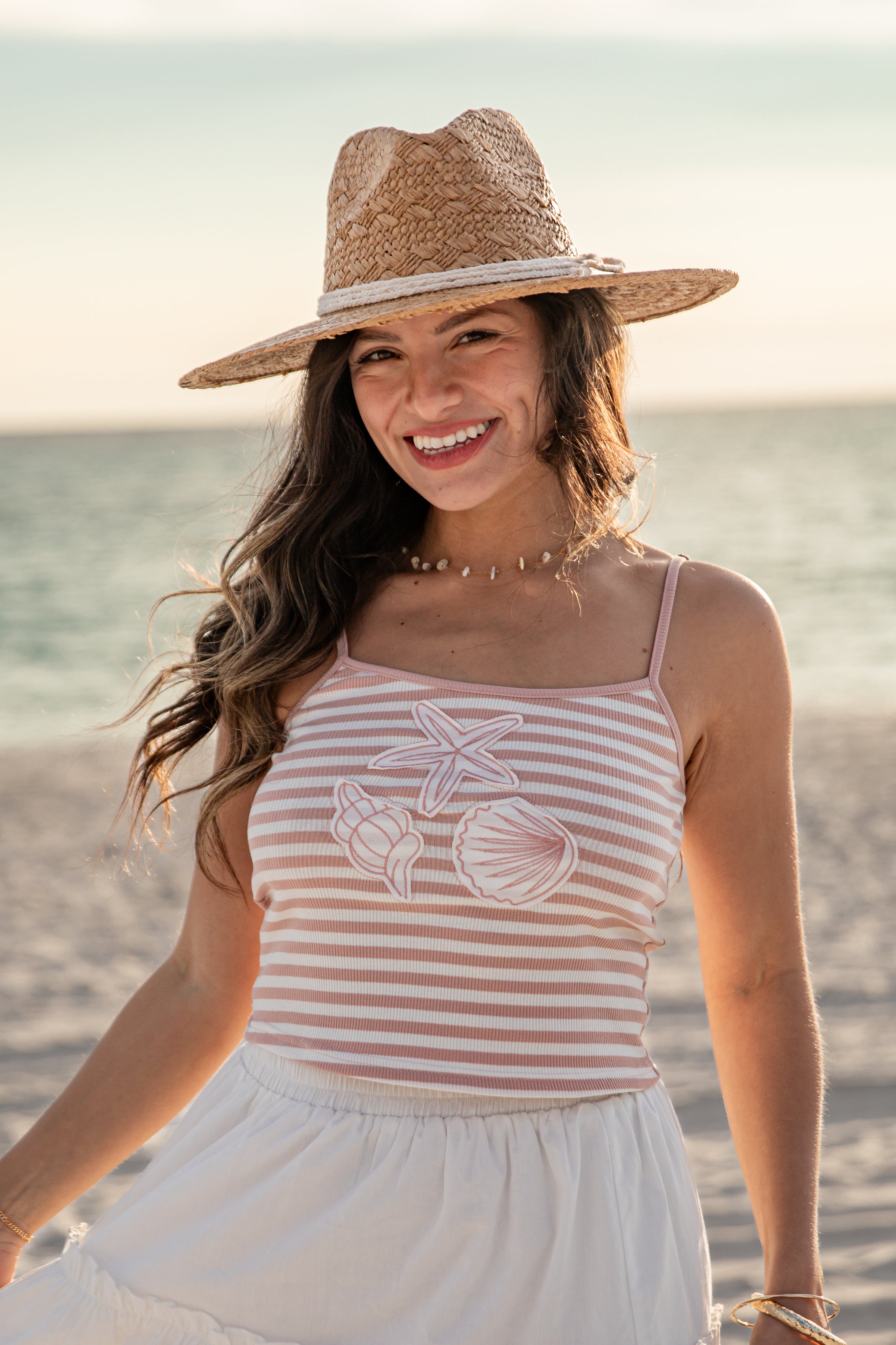 Woman wearing a striped tank top and straw hat on a beach