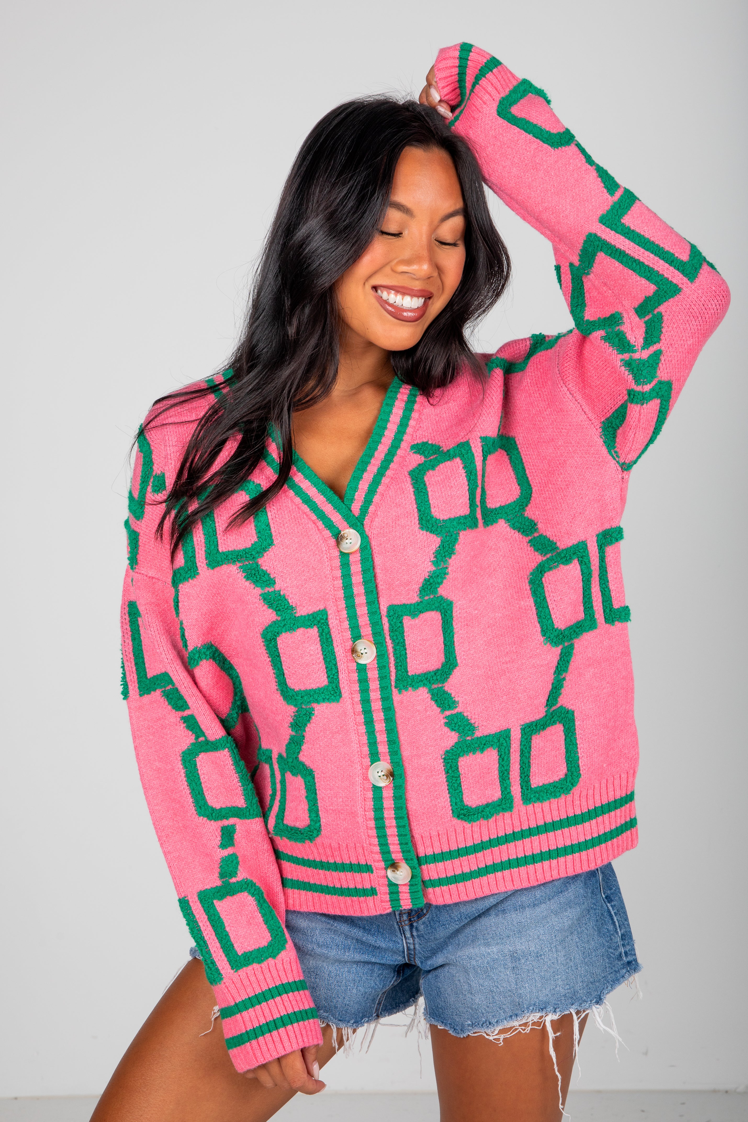 Woman wearing a pink cardigan with green geometric patterns on a gray background