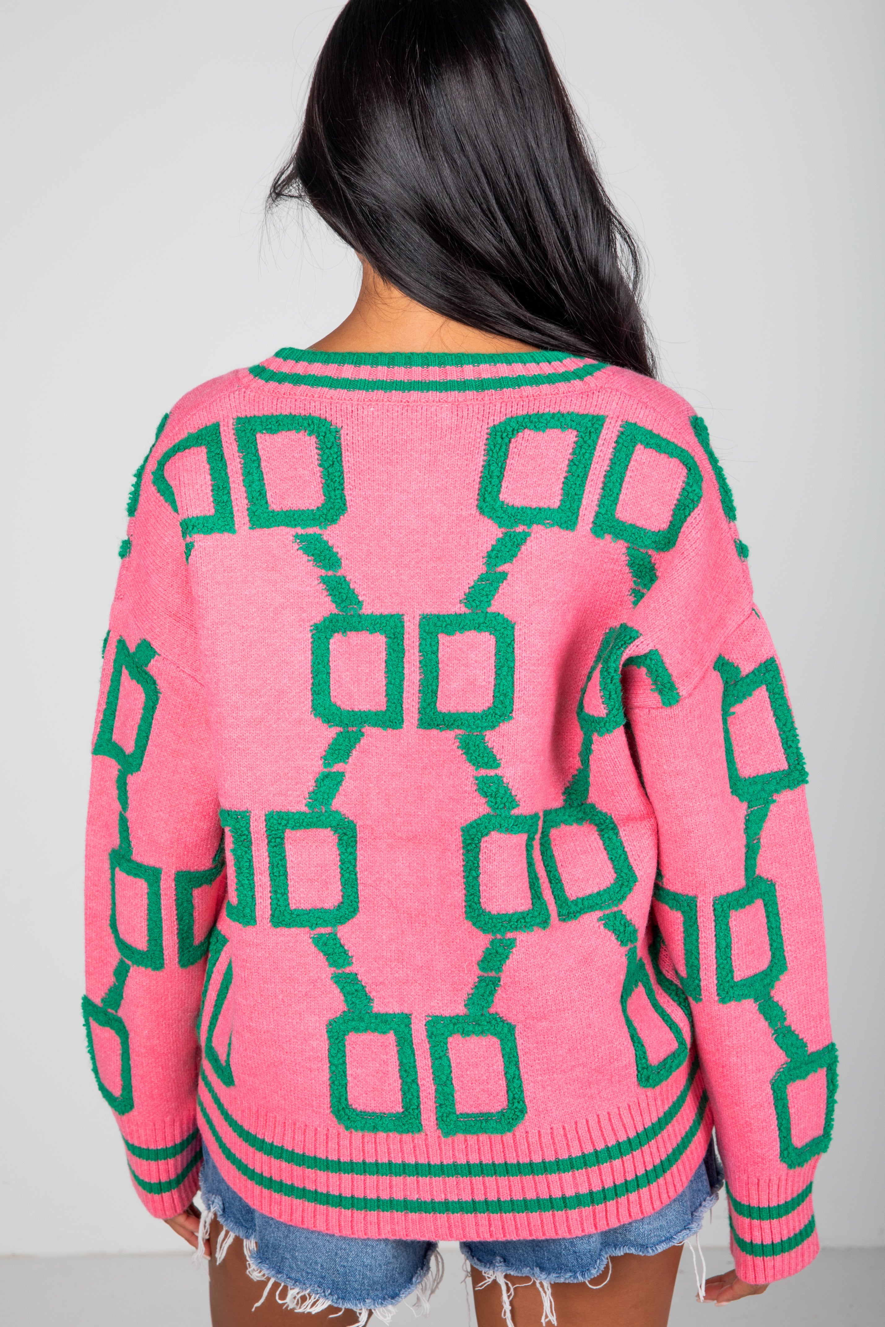 Person wearing a pink sweater with green geometric pattern on a plain background