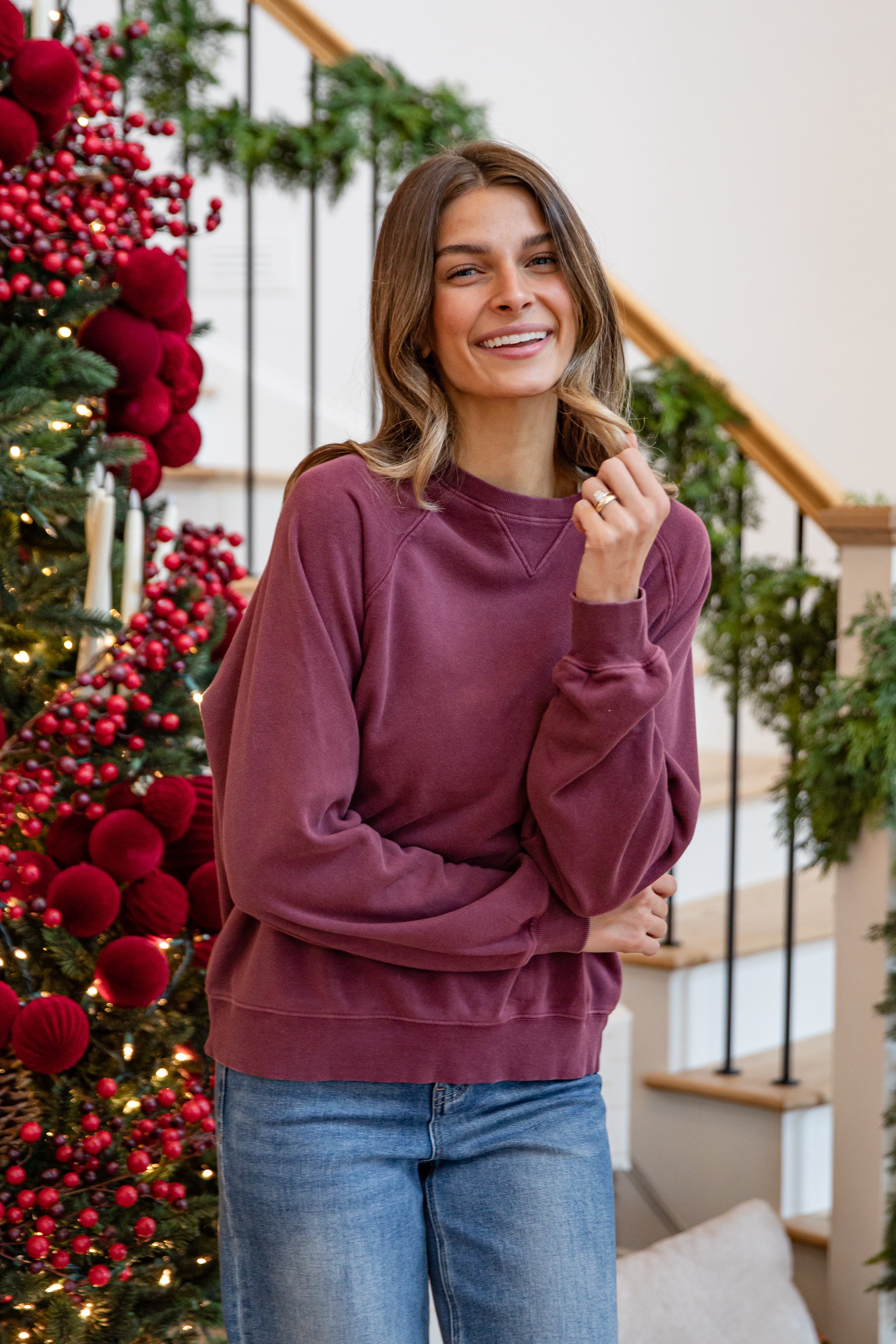 Woman wearing a maroon sweater and blue jeans standing in front of a decorated Christmas tree.