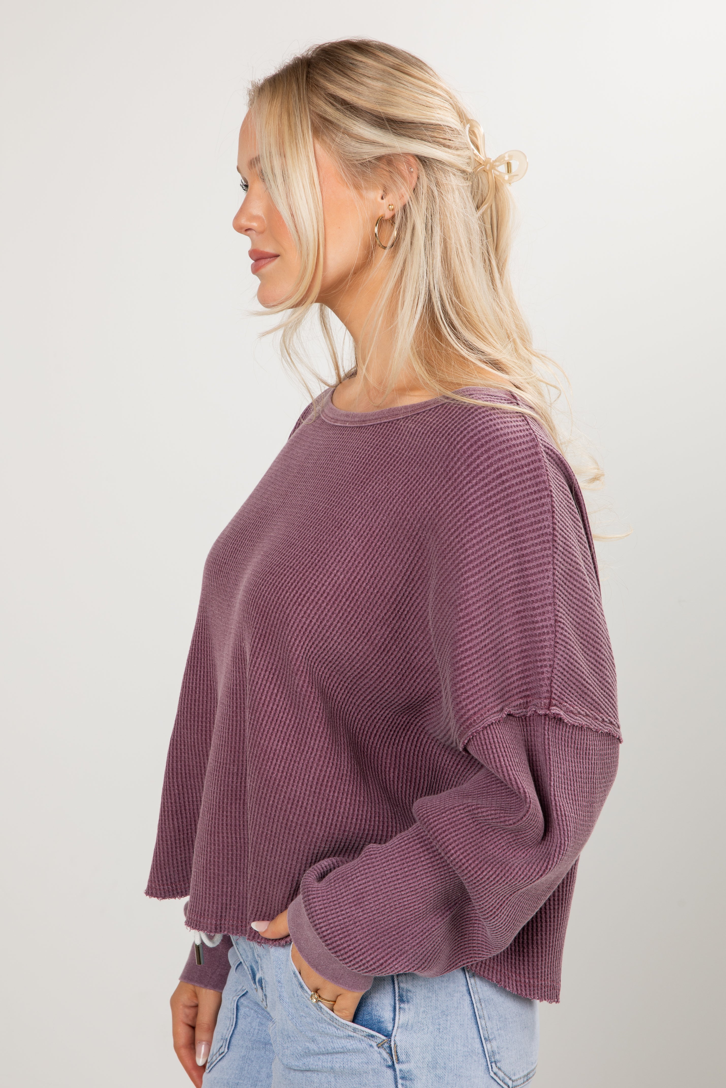 Woman wearing a purple sweater and light blue jeans against a white background