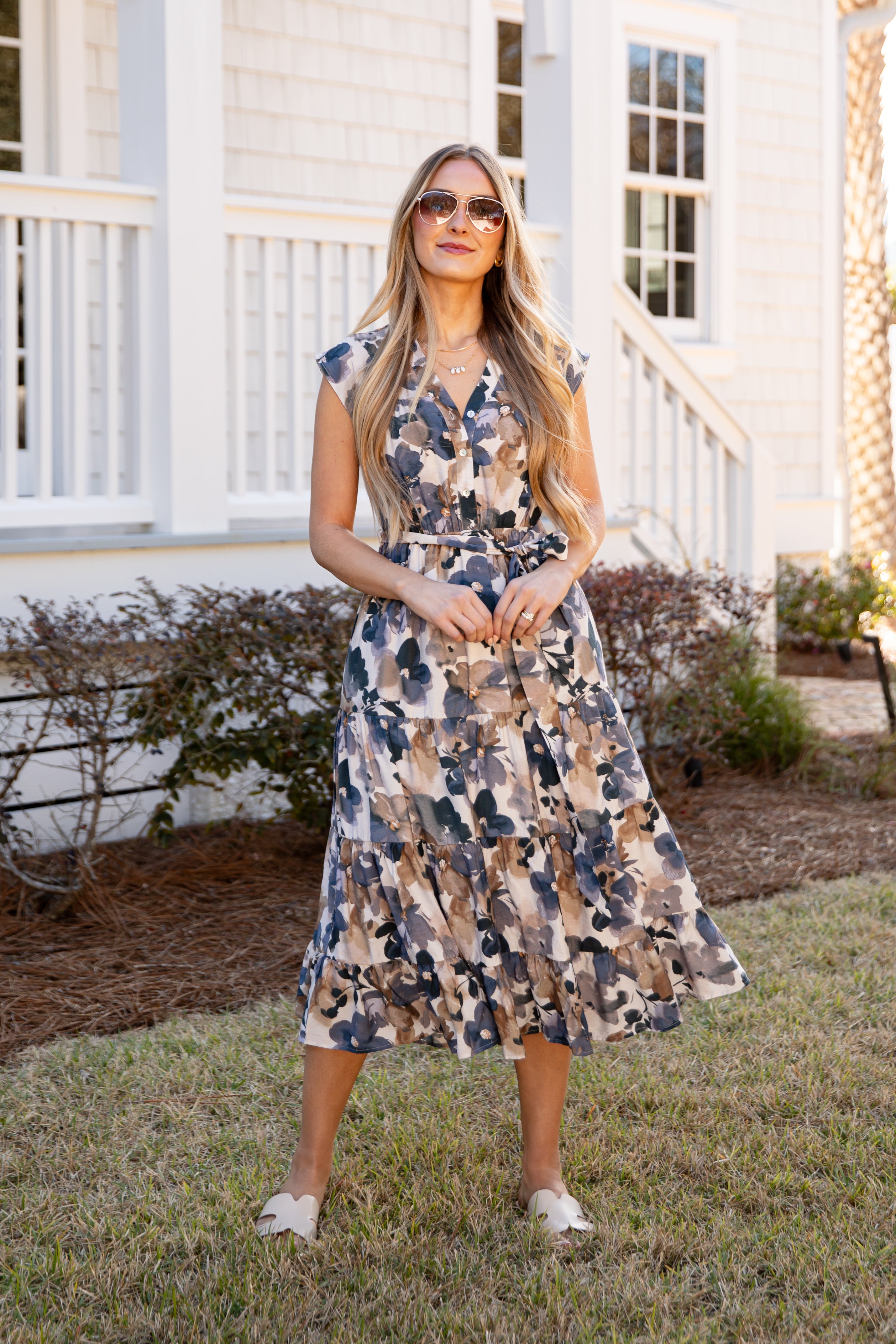 Woman in a floral dress standing in front of a white house.