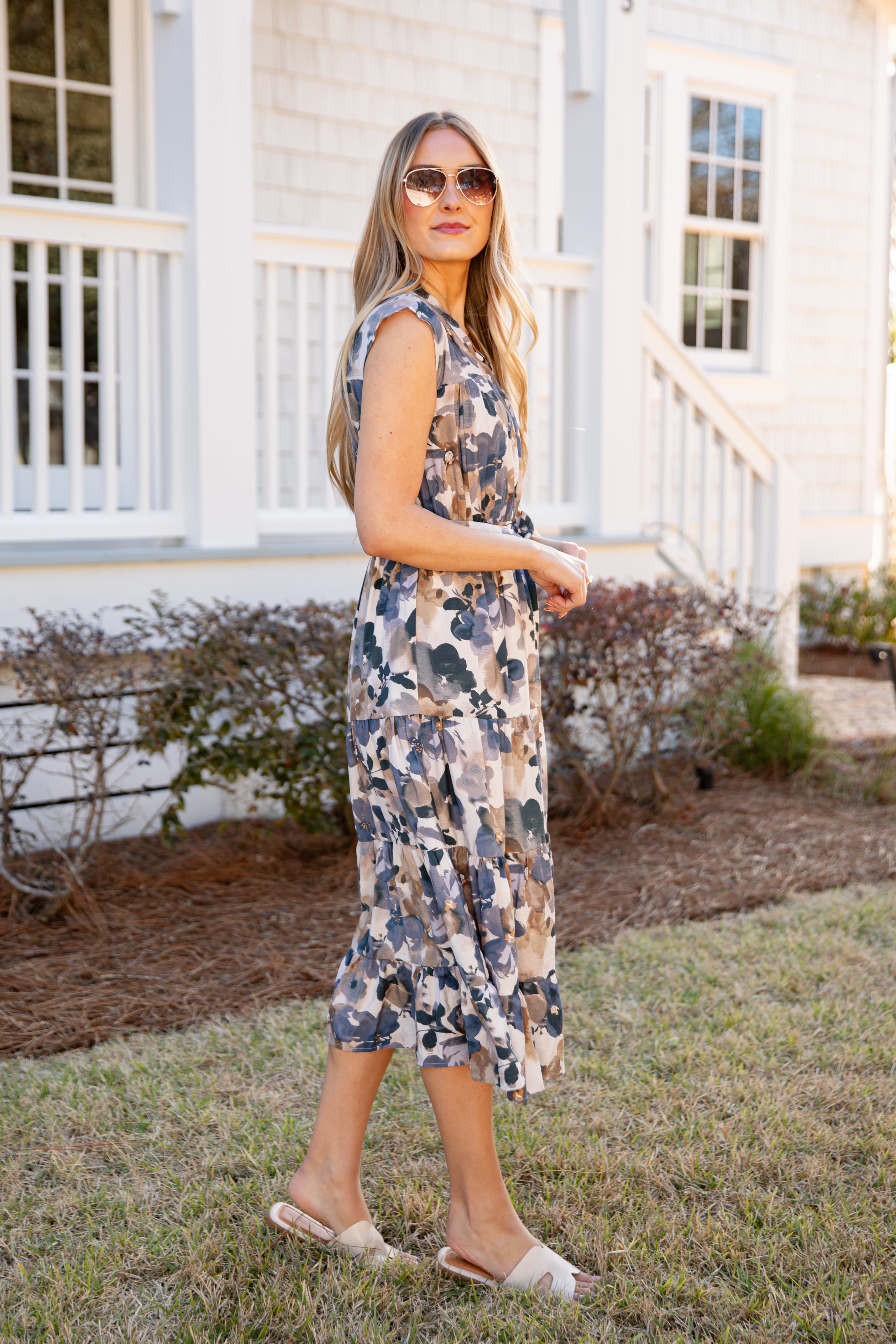 Woman in a floral dress standing in front of a white house.