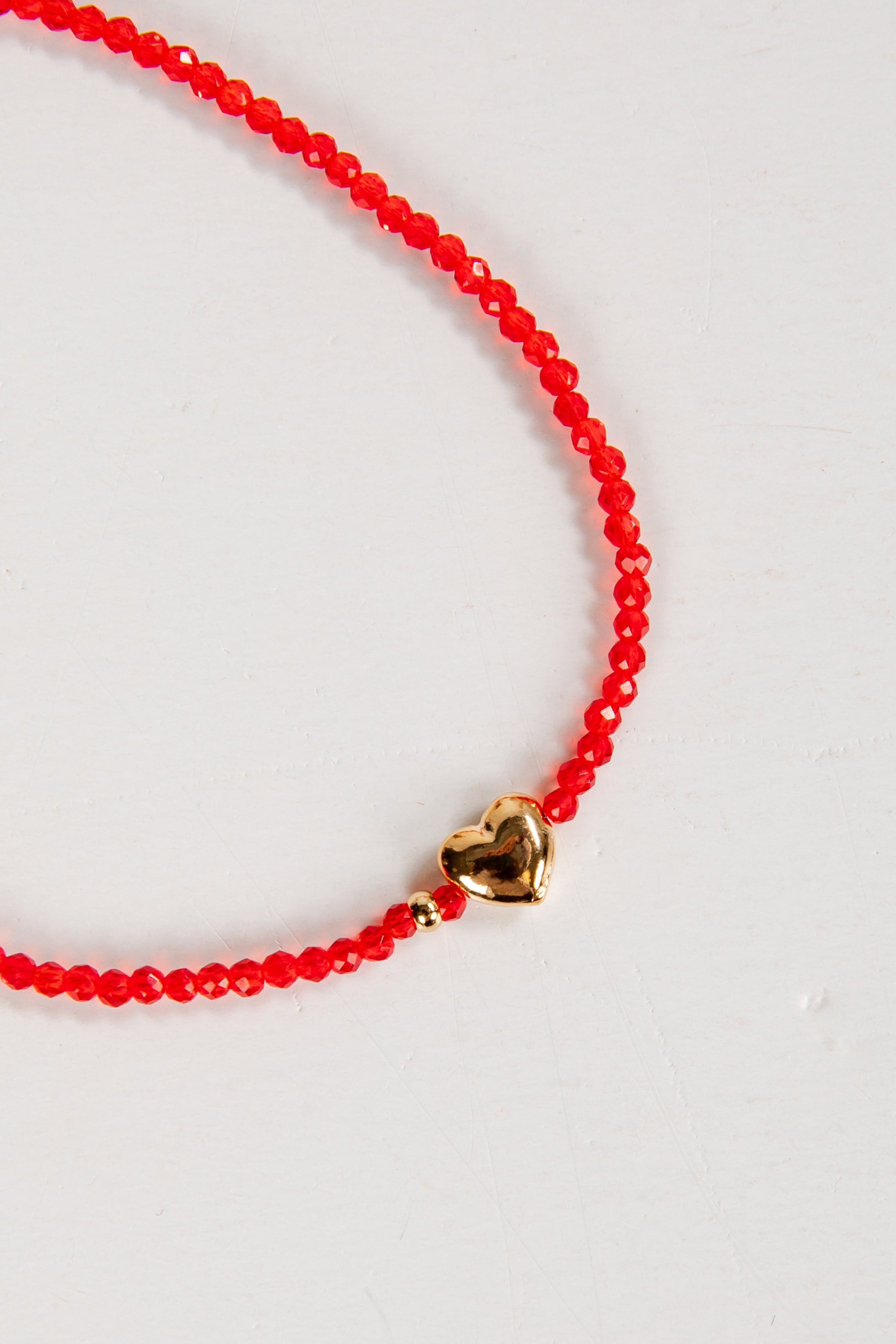 Red beaded necklace with a gold heart charm on a white background