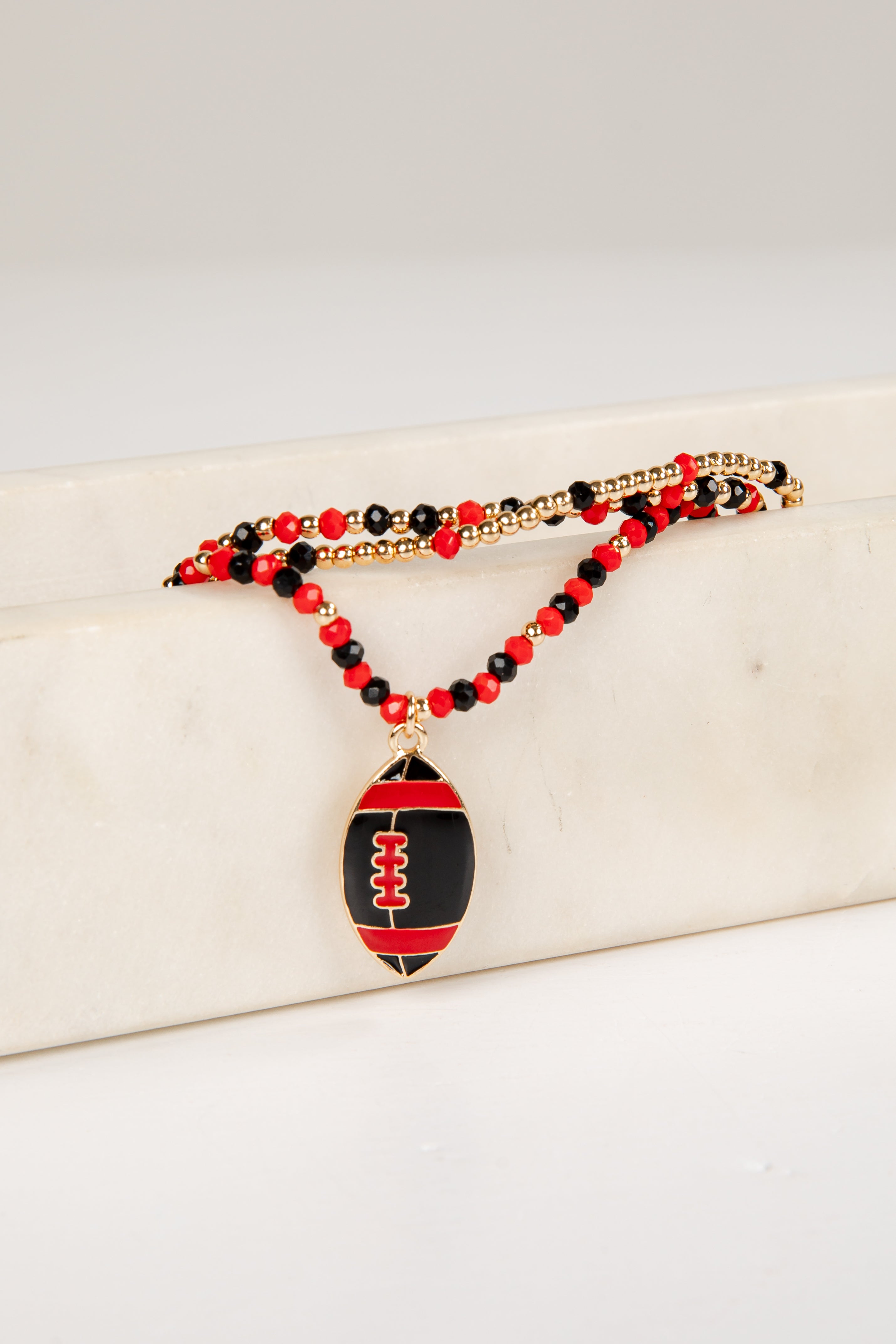 Necklace with football pendant and red and black beads on a white surface