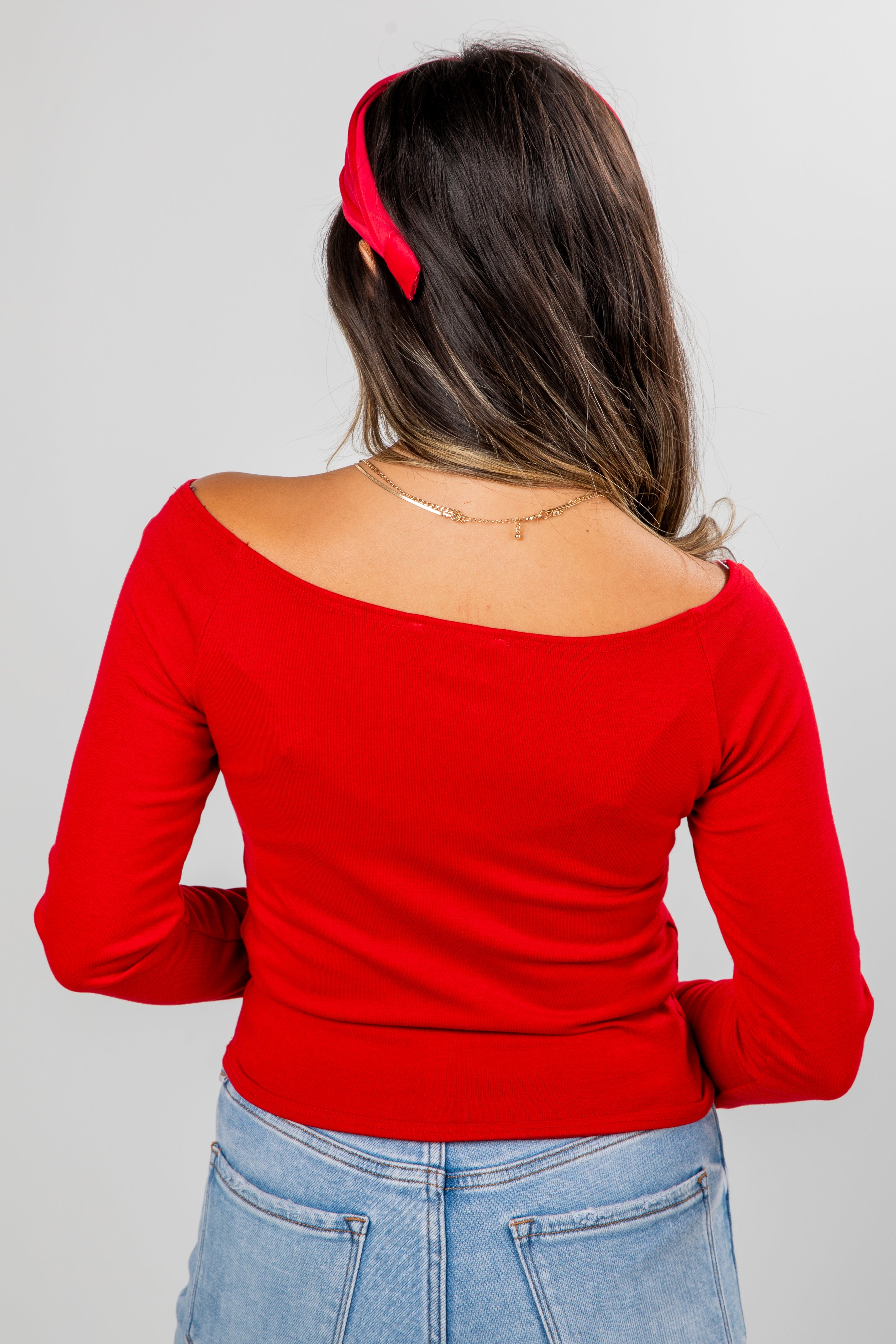 Woman wearing a red top and blue jeans with a red headband on a gray background