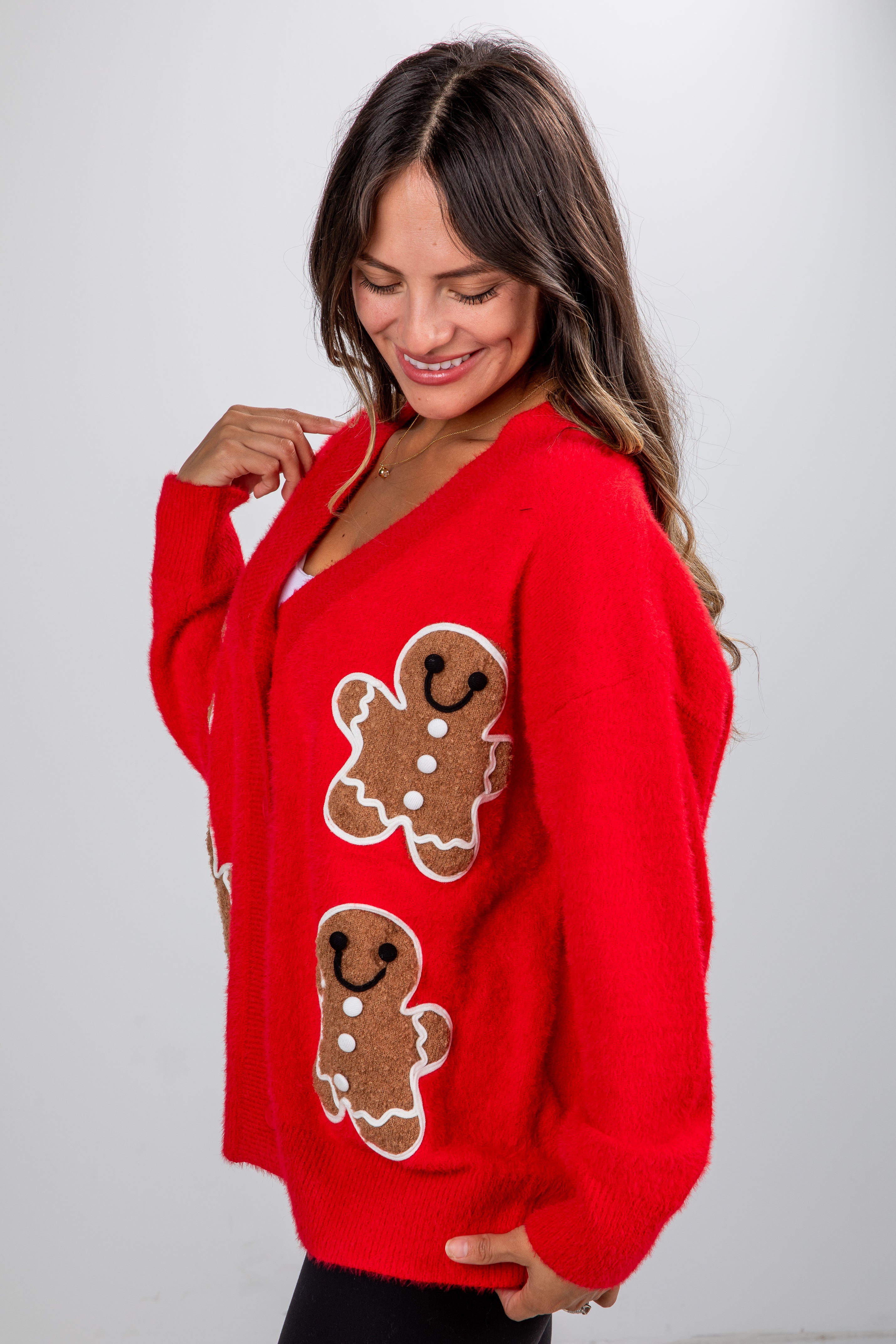Woman wearing a red sweater with gingerbread man designs on a plain background