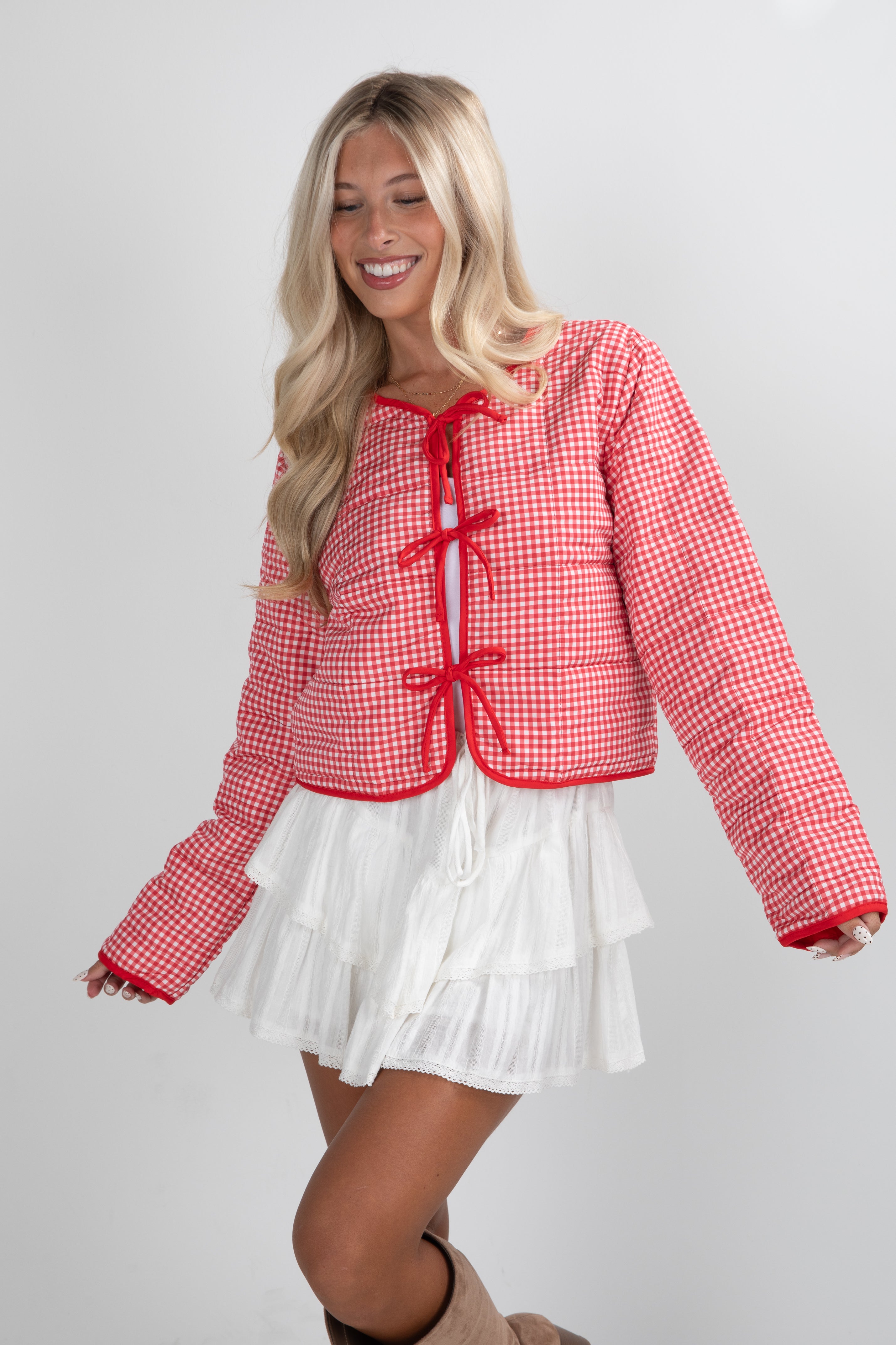Woman wearing a red and white checkered jacket with a white skirt on a gray background
