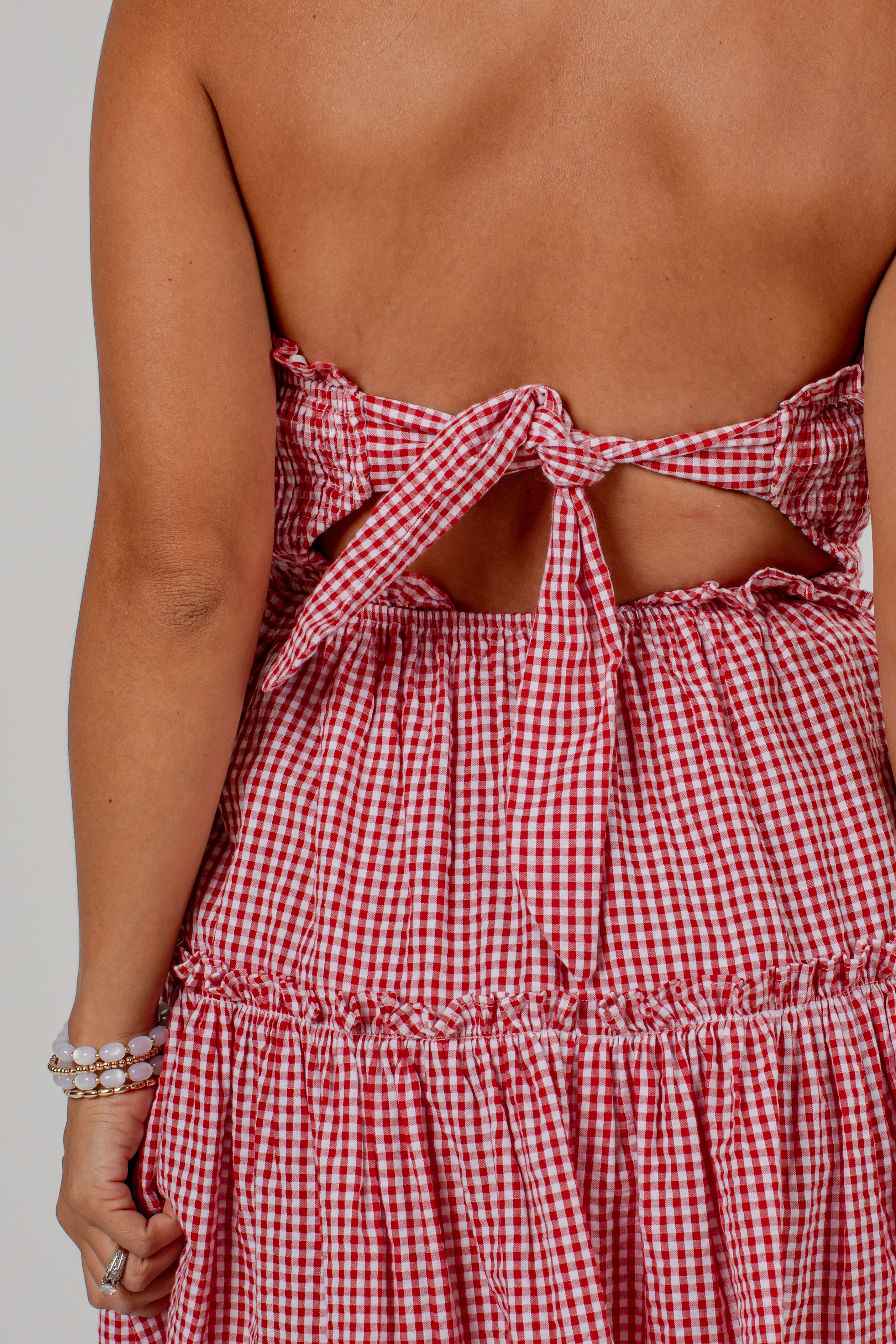 Close-up back view of a woman wearing a red and white gingham dress with a tie-back cutout design.