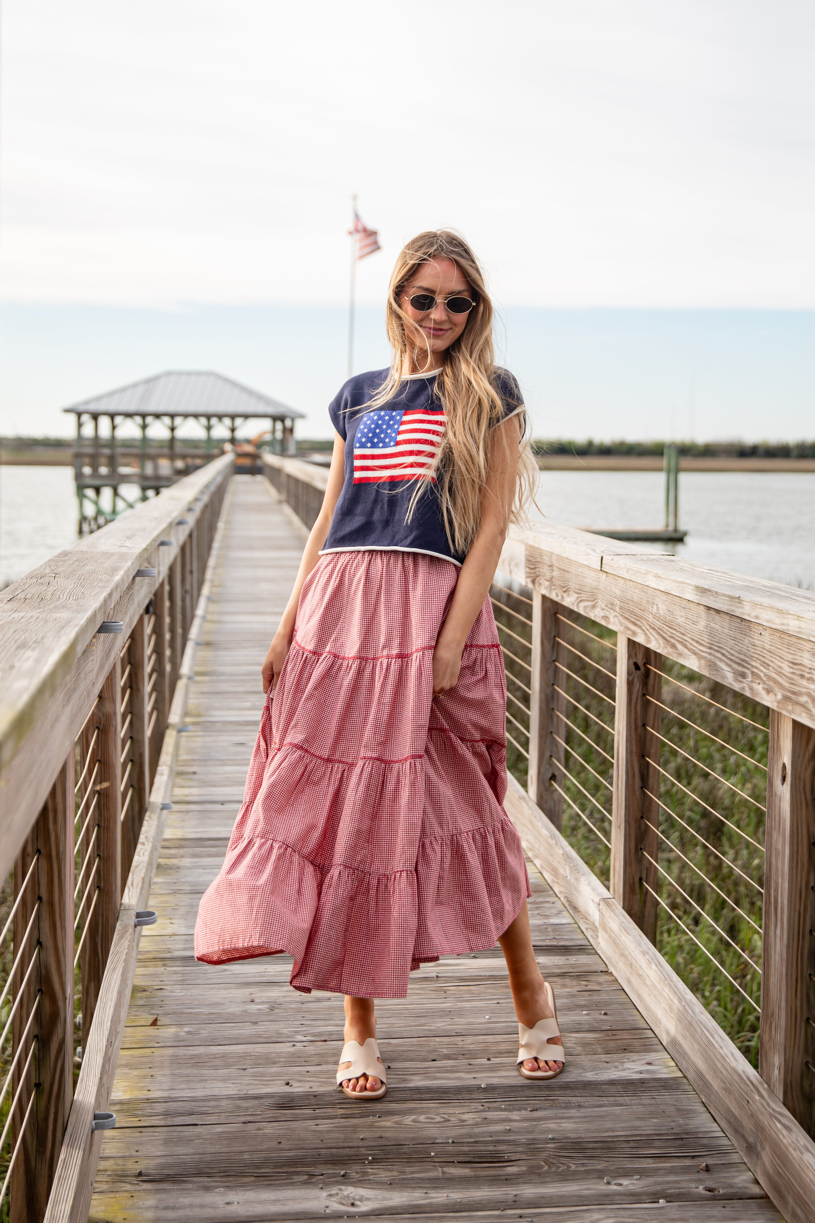 Woman in a pink dress and navy t-shirt with an American flag on a wooden dock.