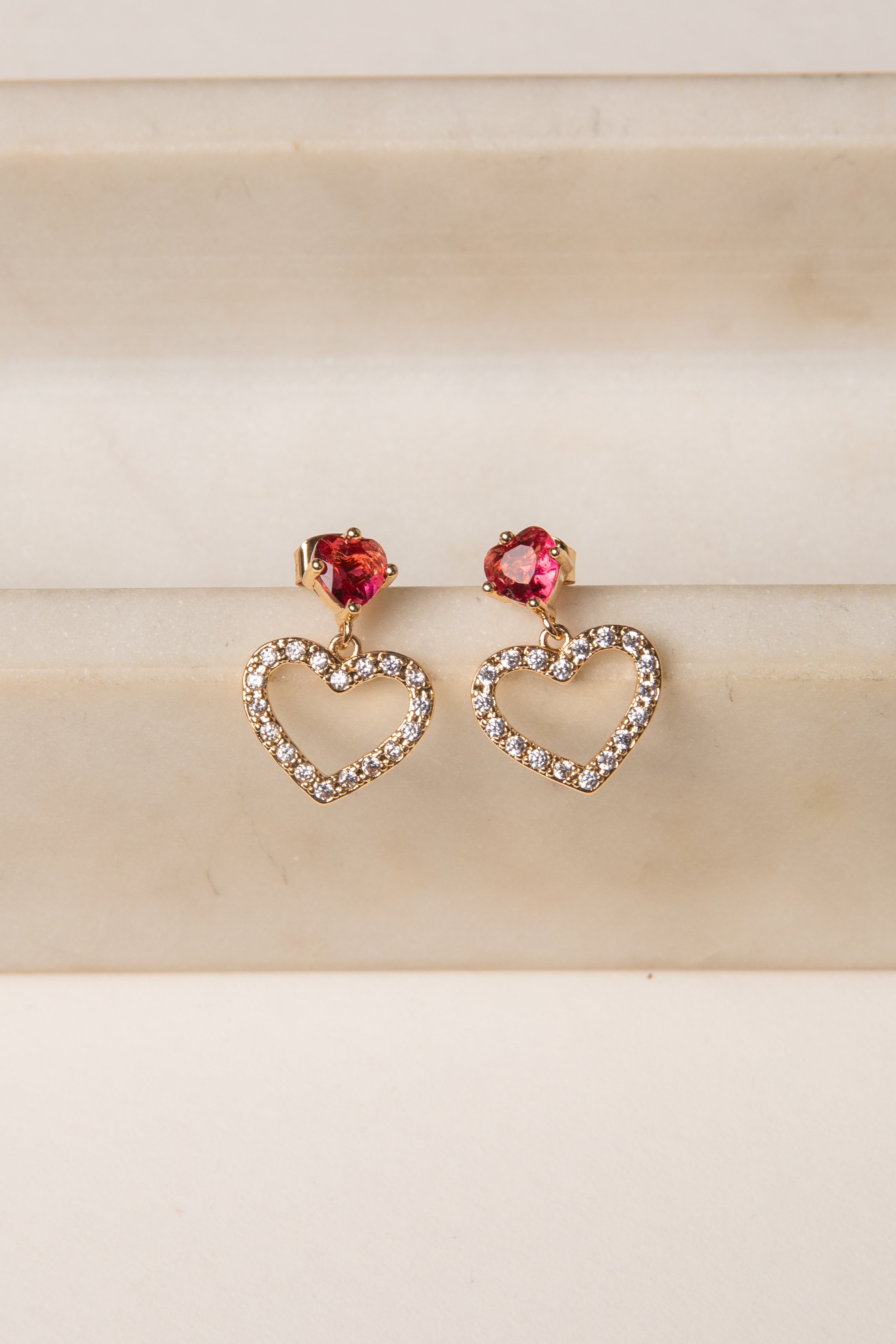 Heart-shaped earrings with red gemstones on a beige background