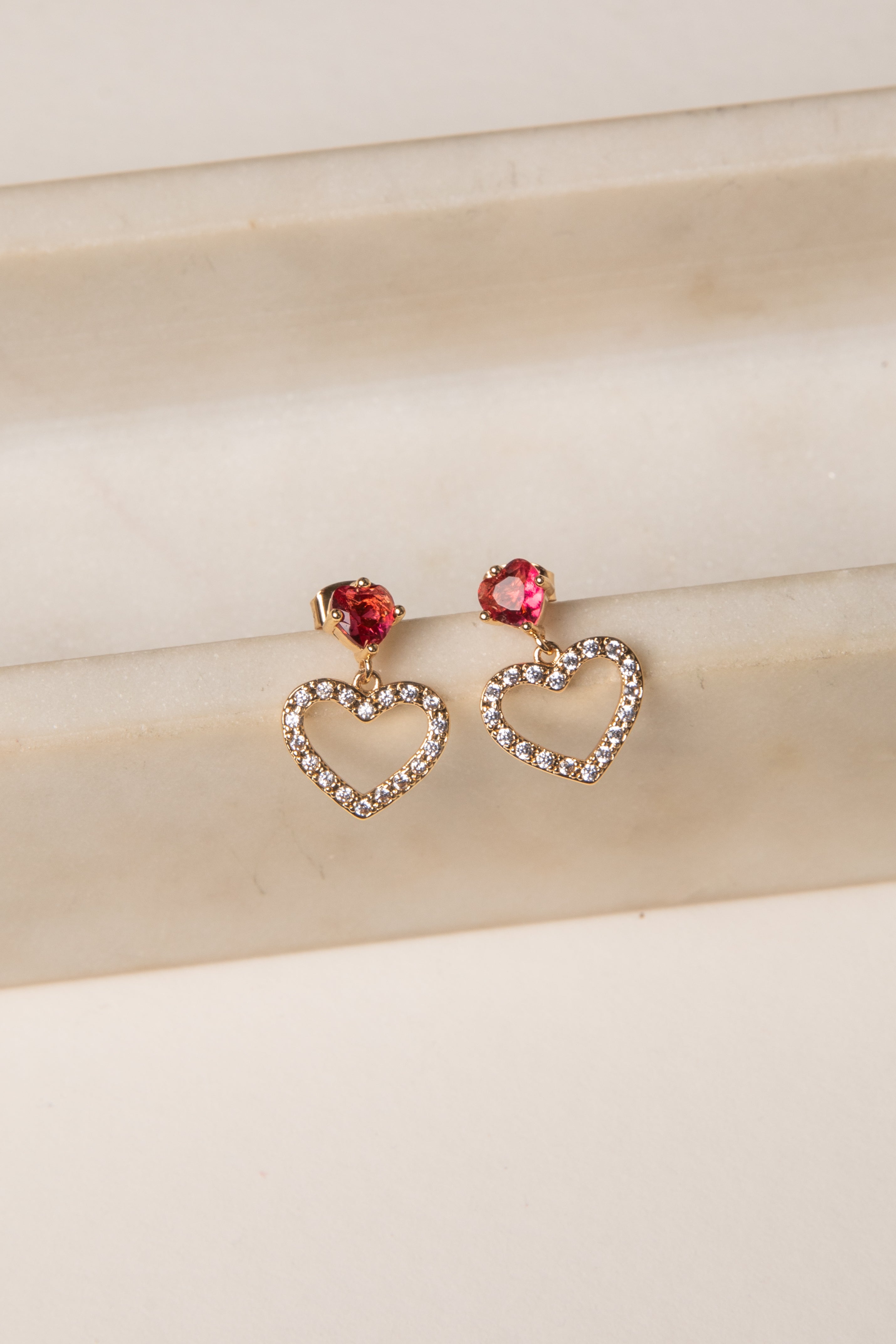 Heart-shaped earrings with red gemstones on a beige fabric background